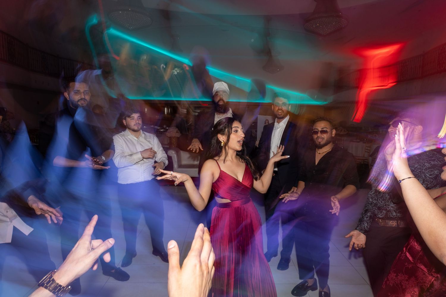 People dancing and celebrating on a dance floor illuminated by colorful red and blue lights at a nightclub party.