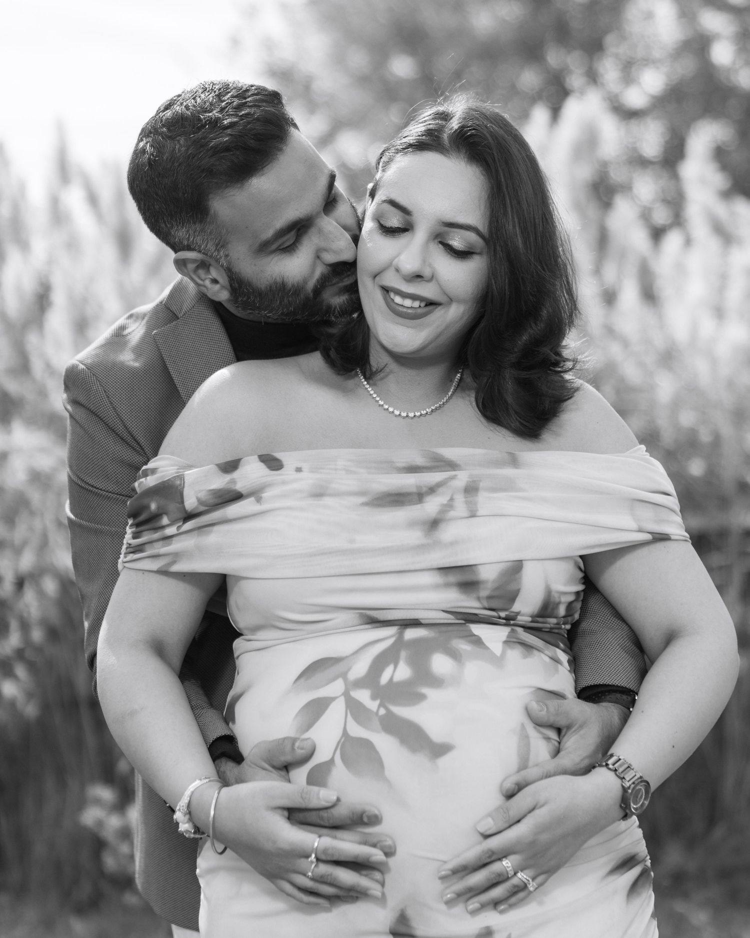 A tender black and white maternity portrait of a couple embracing outdoors in natural lighting.
