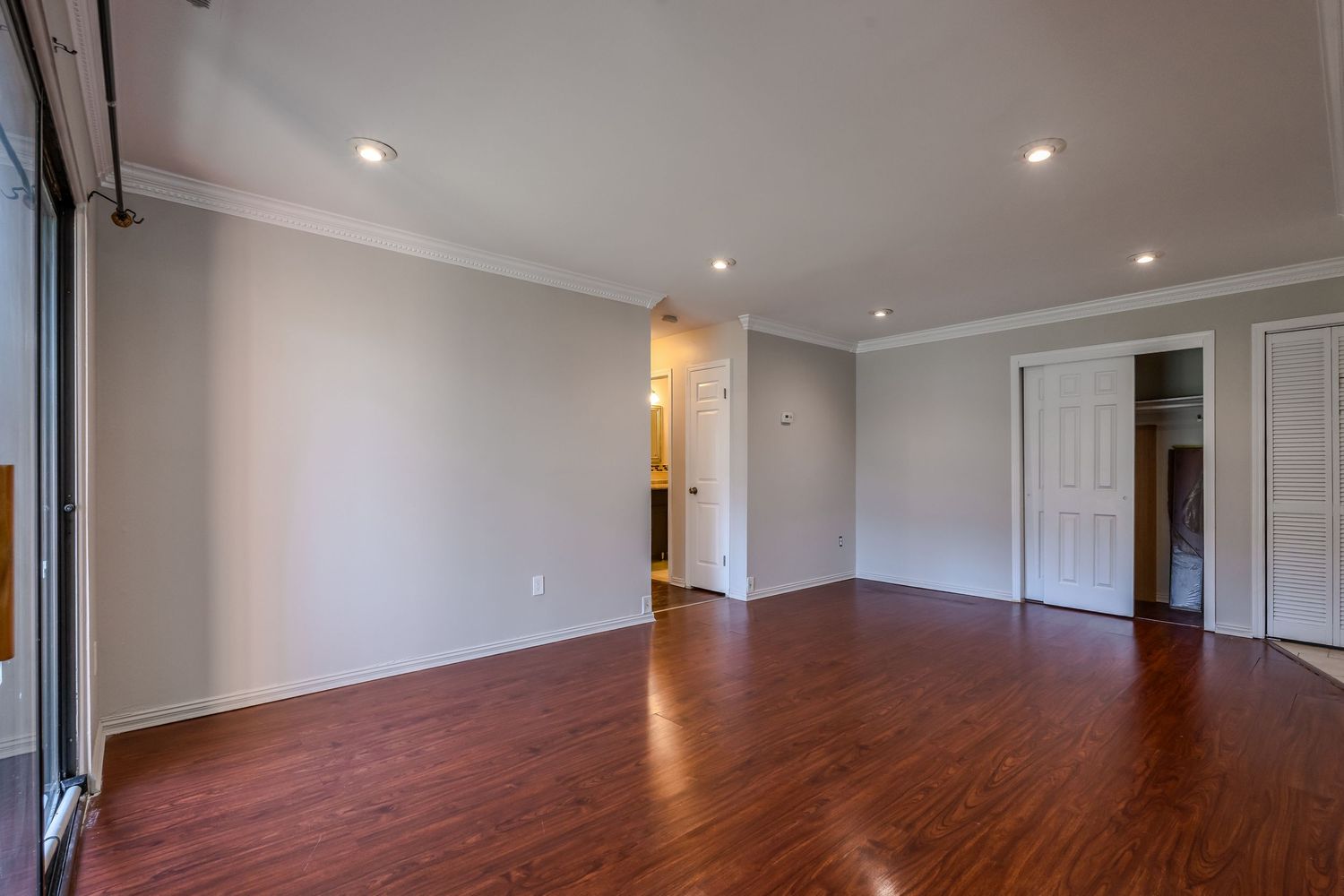 A modern empty room with hardwood floors, recessed lighting, and white walls stretching down a long hallway.