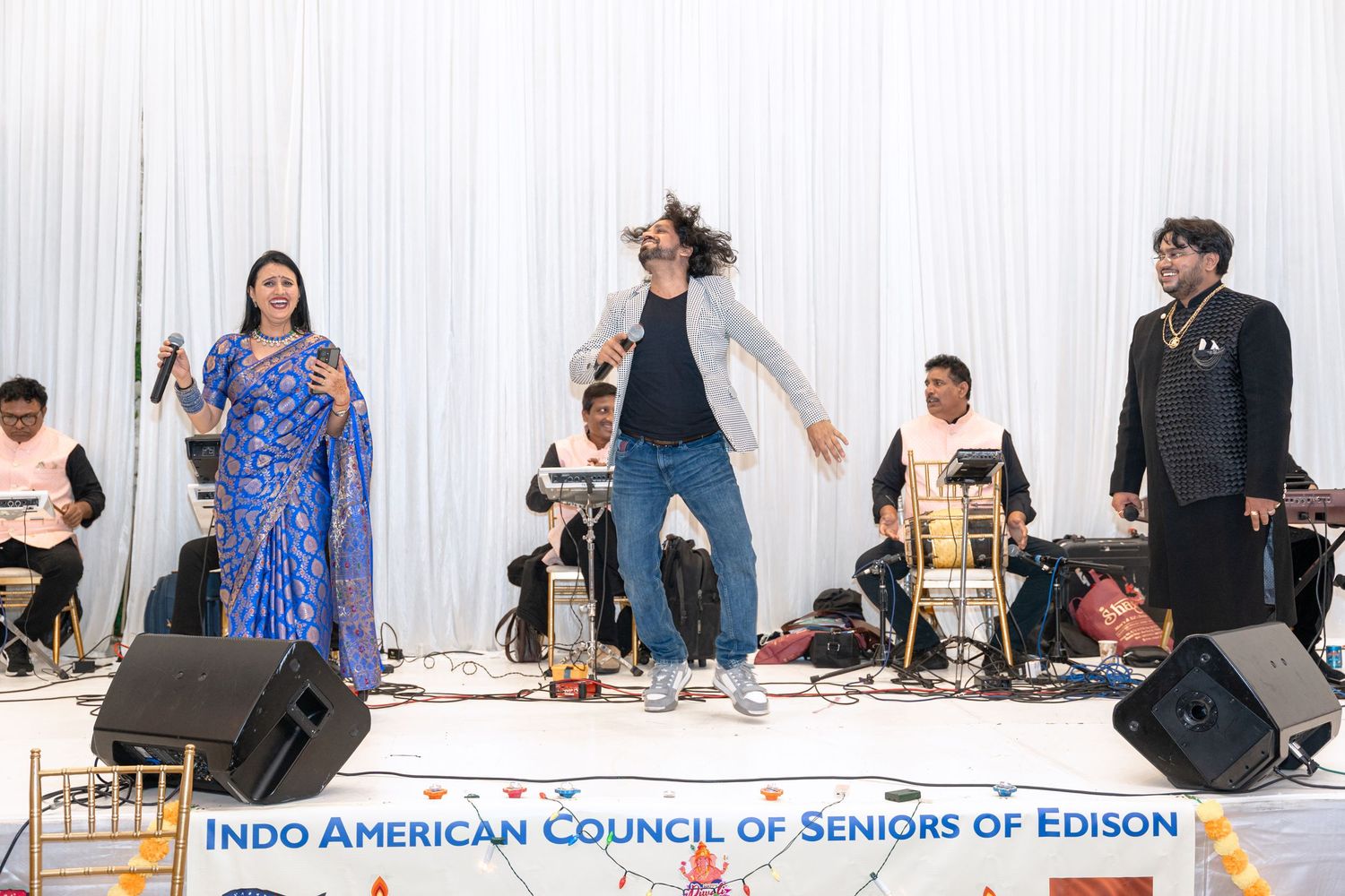 A diverse group of people gathered at tables during a community event with banners and decorations visible.