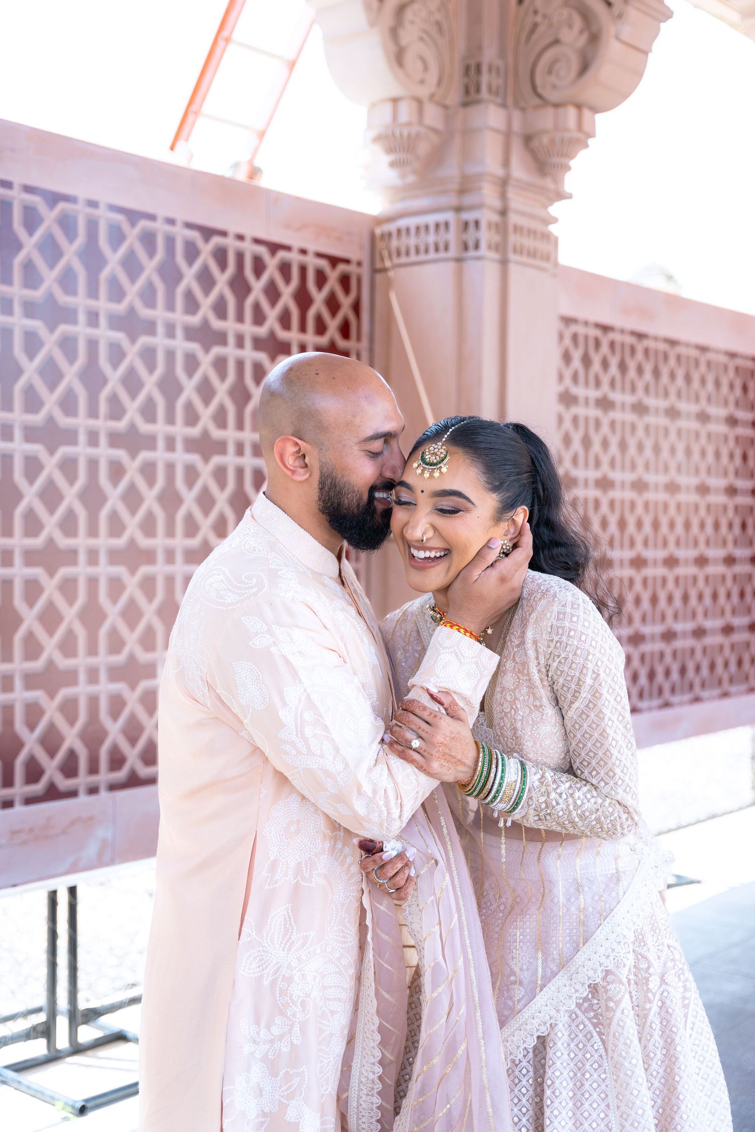 Romantic couple in white outfits share intimate moments at ornate architectural setting.