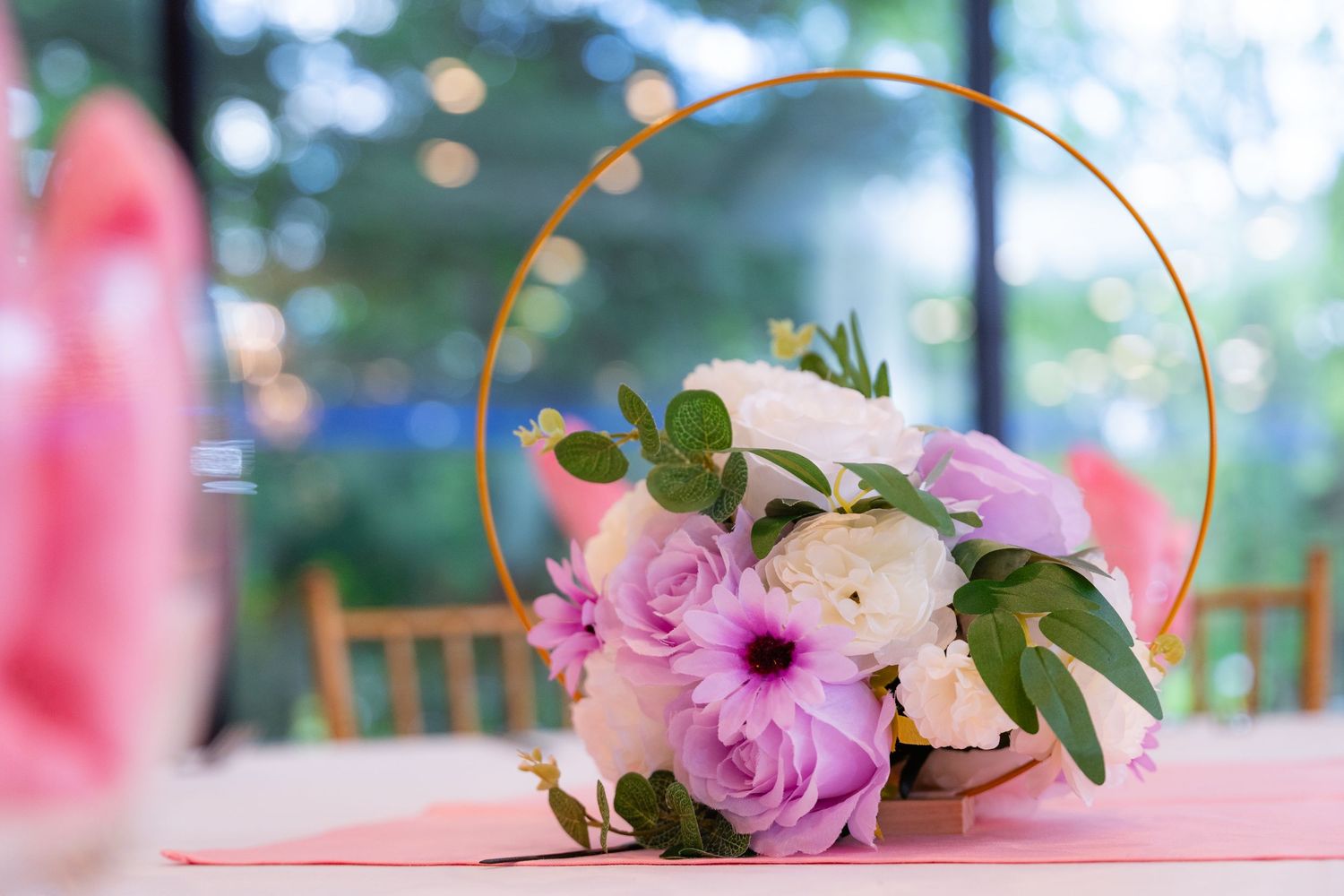 Gold hoop centerpiece with pink and purple flowers on pink tablecloth.