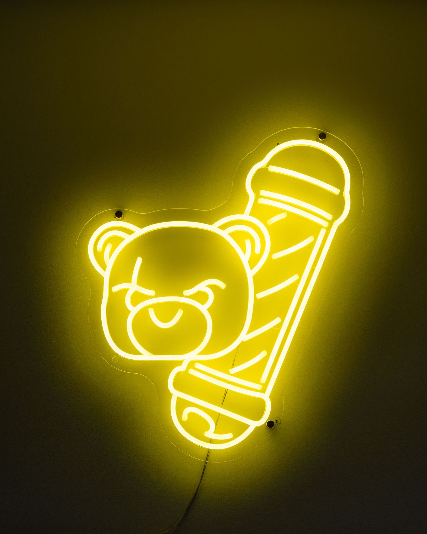 Yellow neon sign shaped like a teddy bear with a barber pole in a dark room.