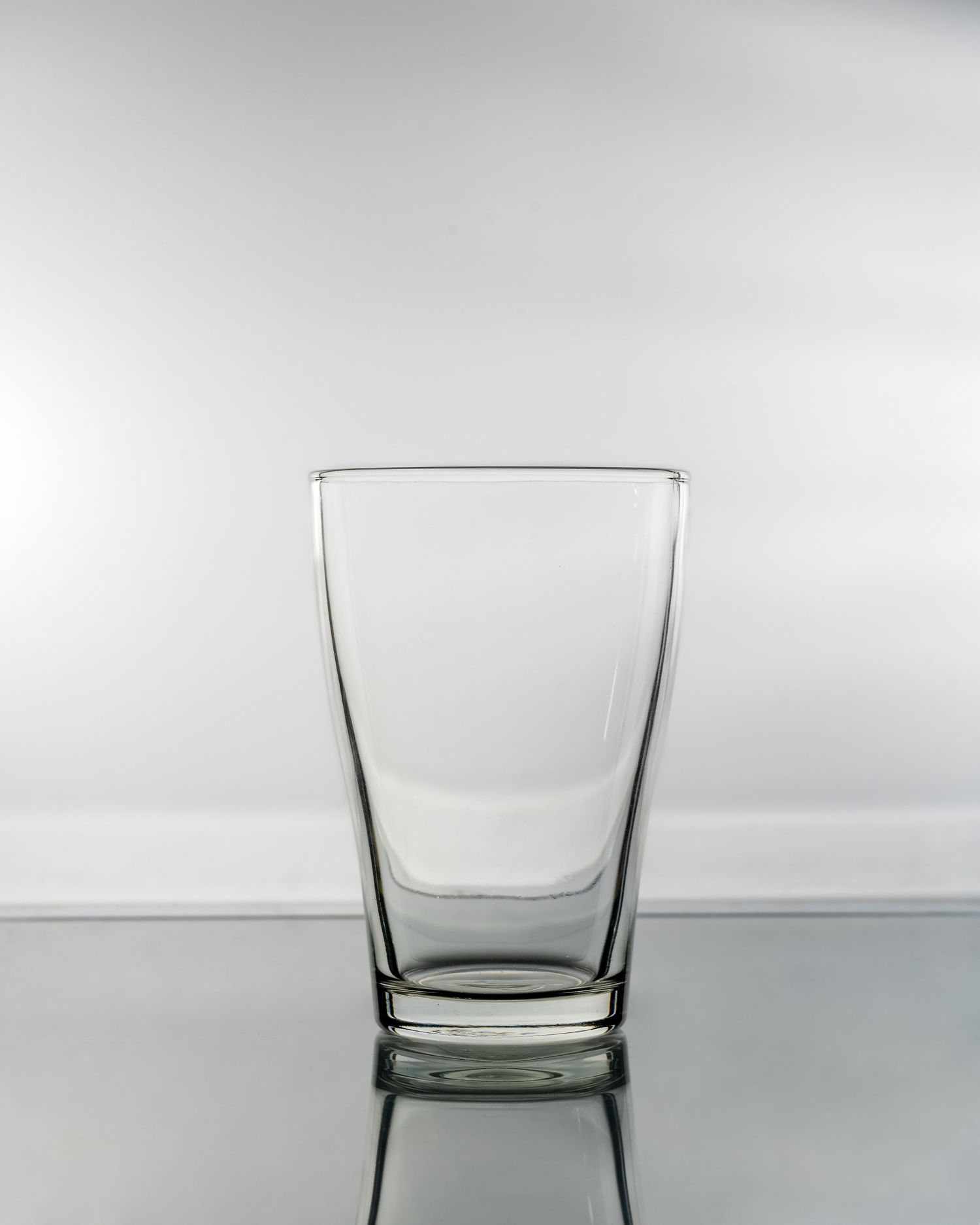 Empty lowball whiskey glass on reflective surface with minimalist lighting and clean background.