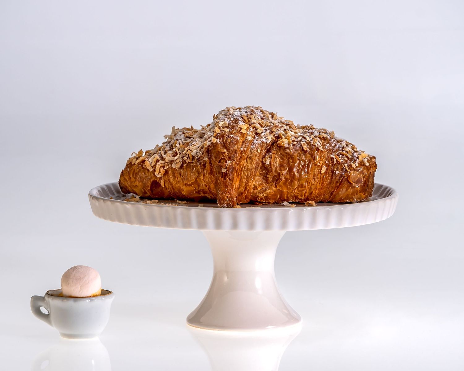 Freshly baked pastries and desserts displayed on elegant white cake stands against a light background.