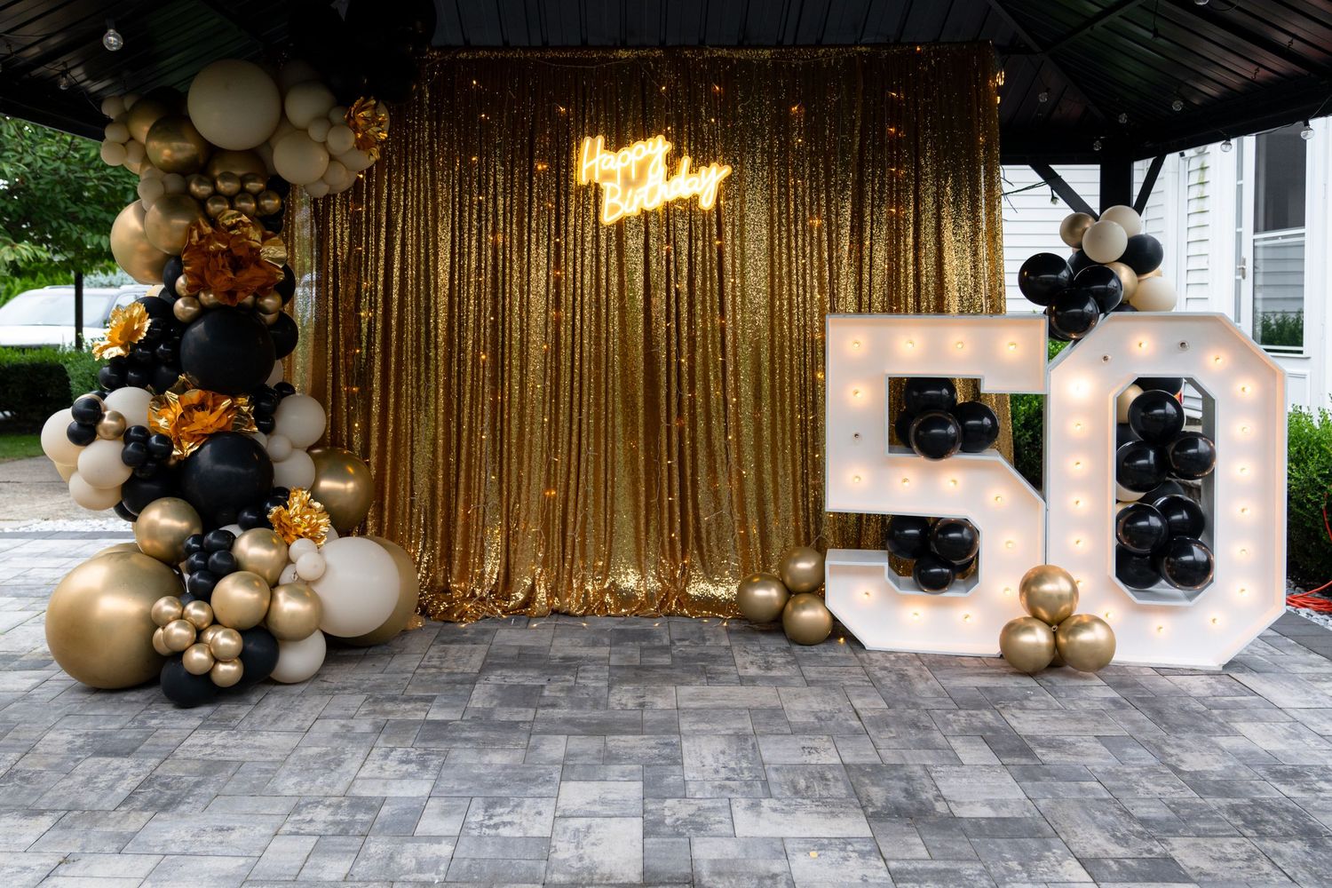 Elegant balloon garland installation with gold, black and white balloons decorating an outdoor patio space.