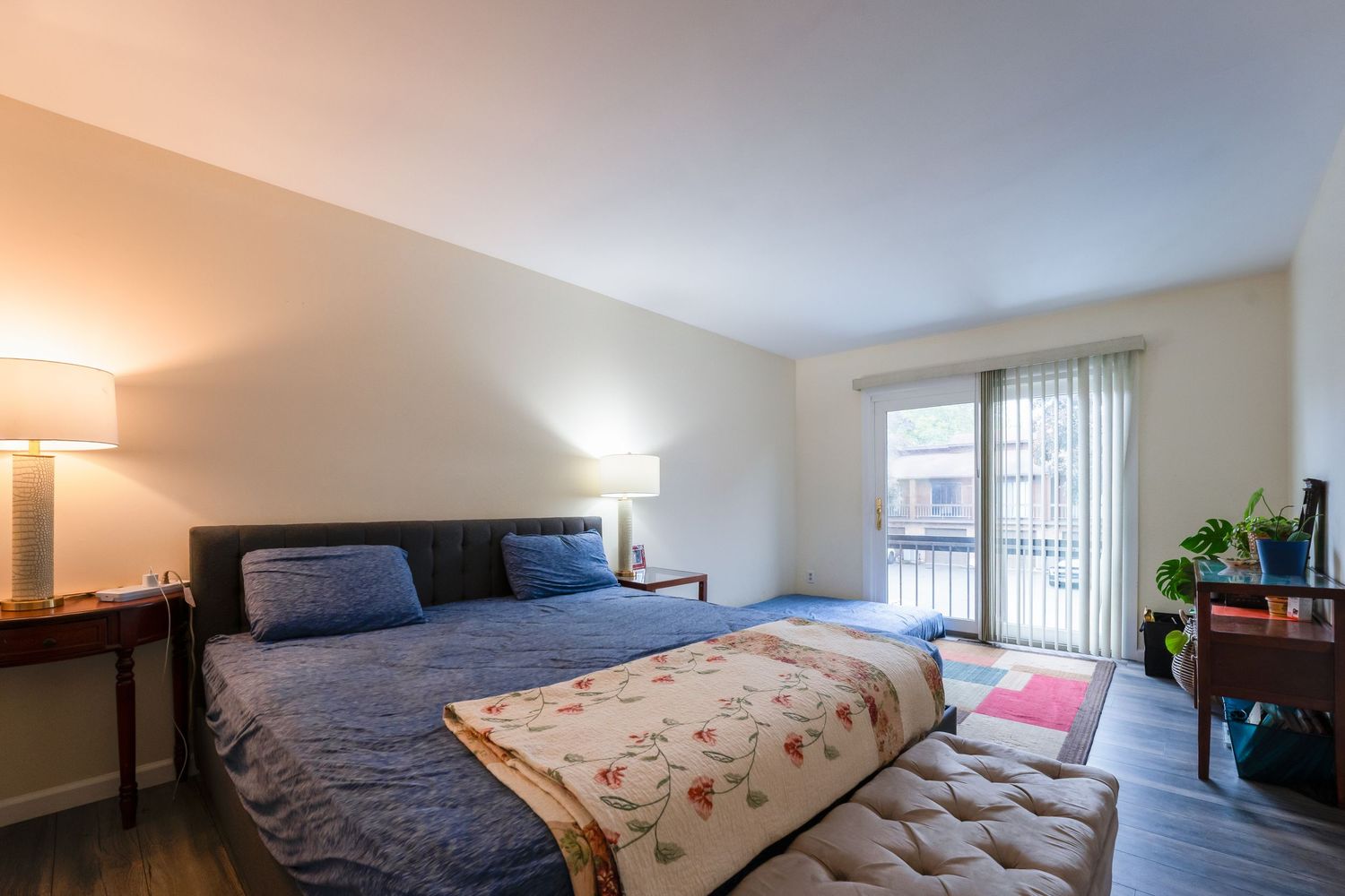 Spacious bedroom with sliding glass door, blue bedding, side table lamp, and natural lighting from patio access.