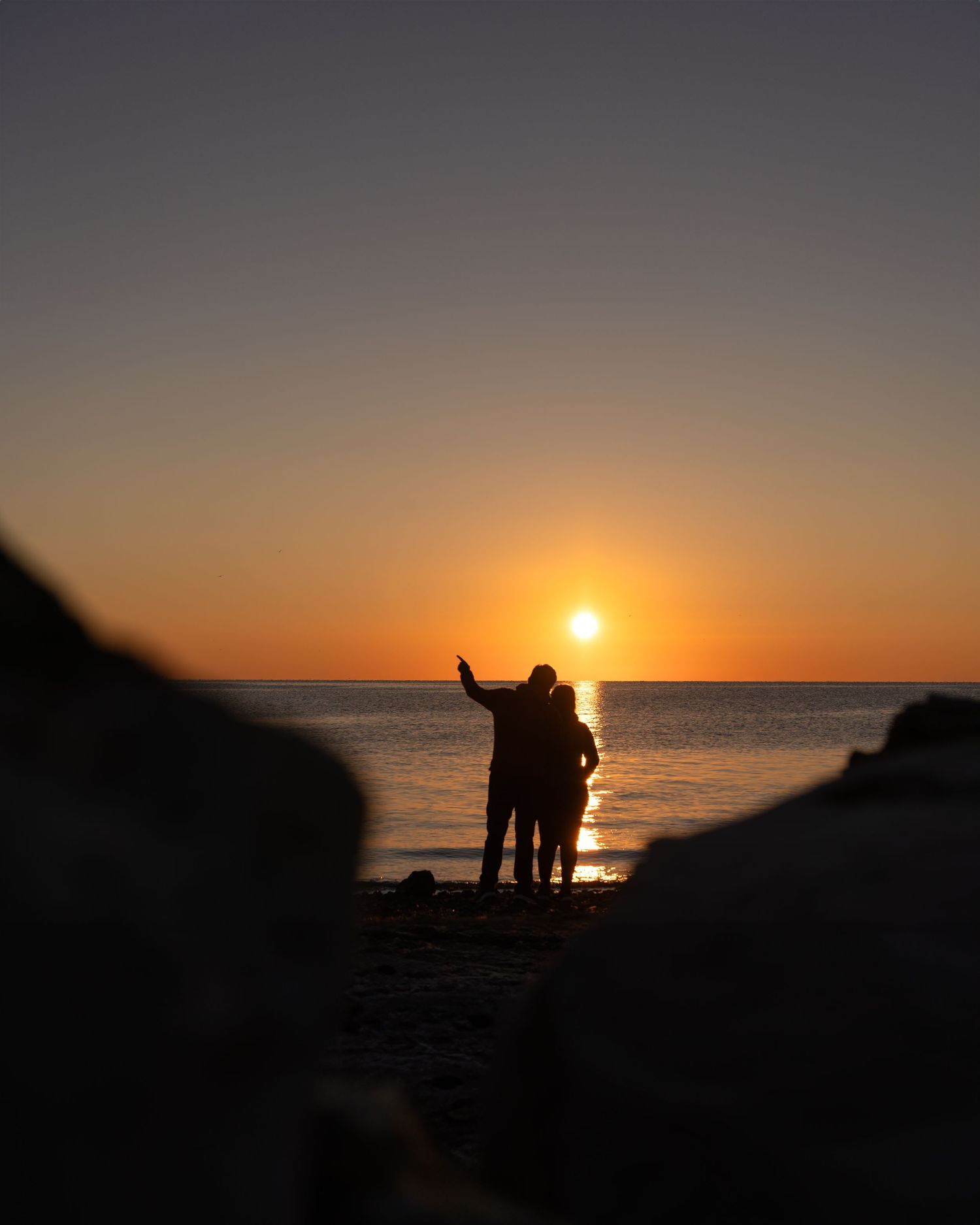 Silhouettes of people watching a vibrant orange sunset over the ocean horizon.