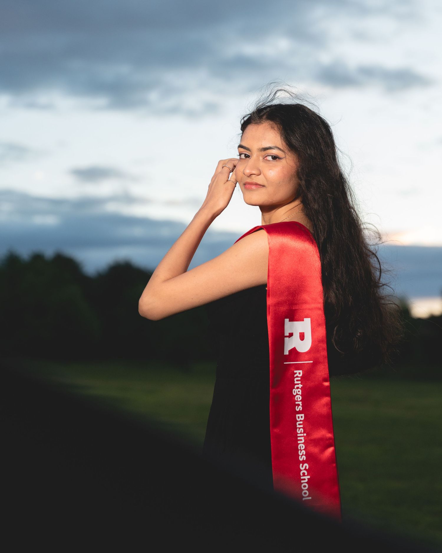 Dramatic sunset portrait with red graduation stole against cloudy sky.