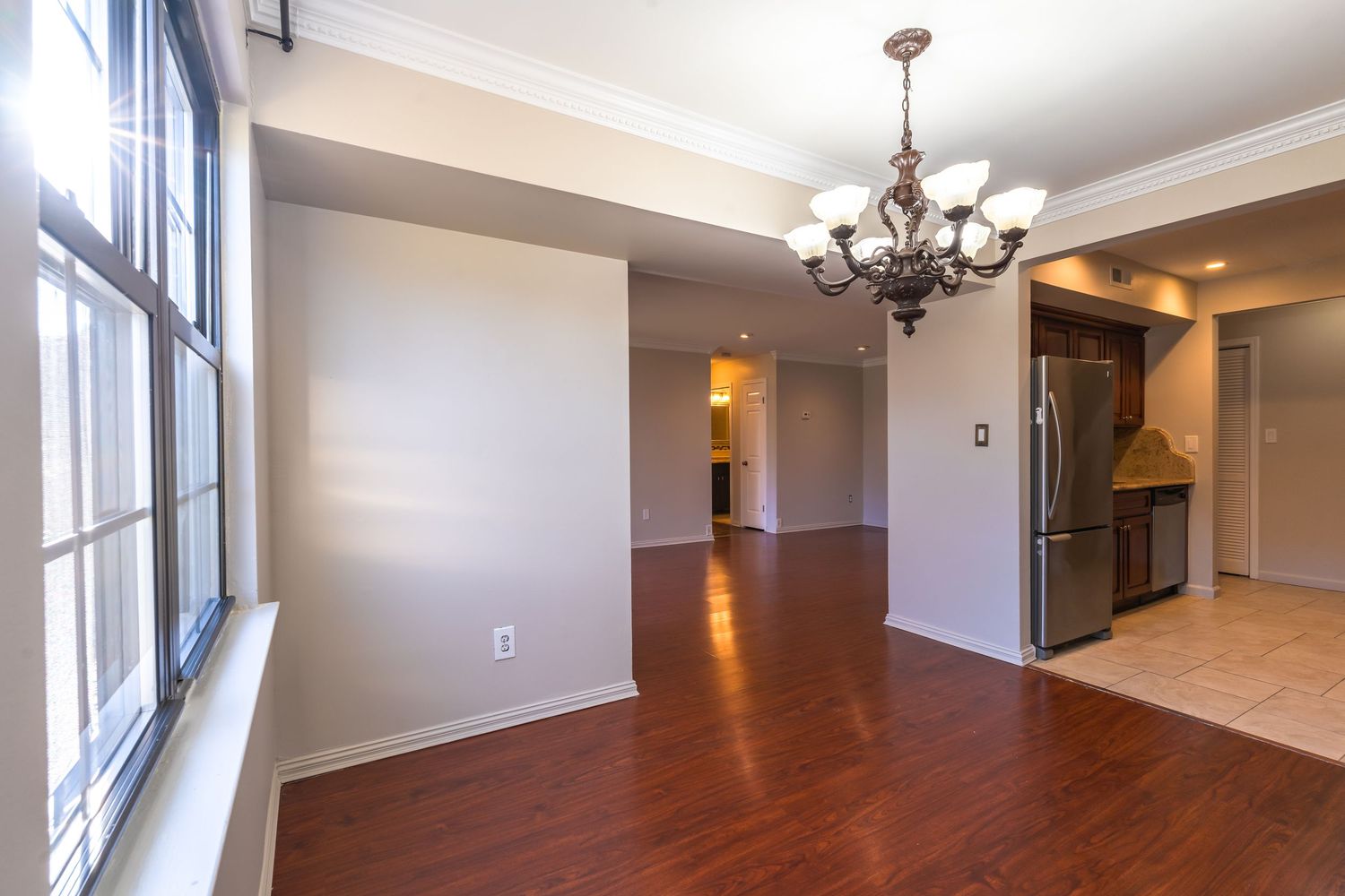 Modern apartment interior features crown molding, recessed lighting, and elegant chandelier in a bright open-concept space.