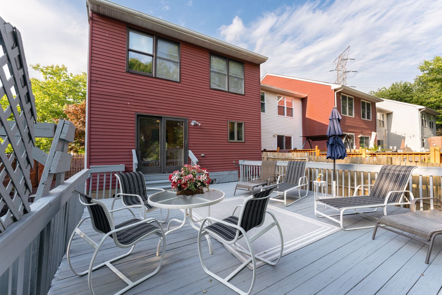 A sunny outdoor deck space with patio furniture including metal chairs, railings and plants in burgundy-colored surroundings.