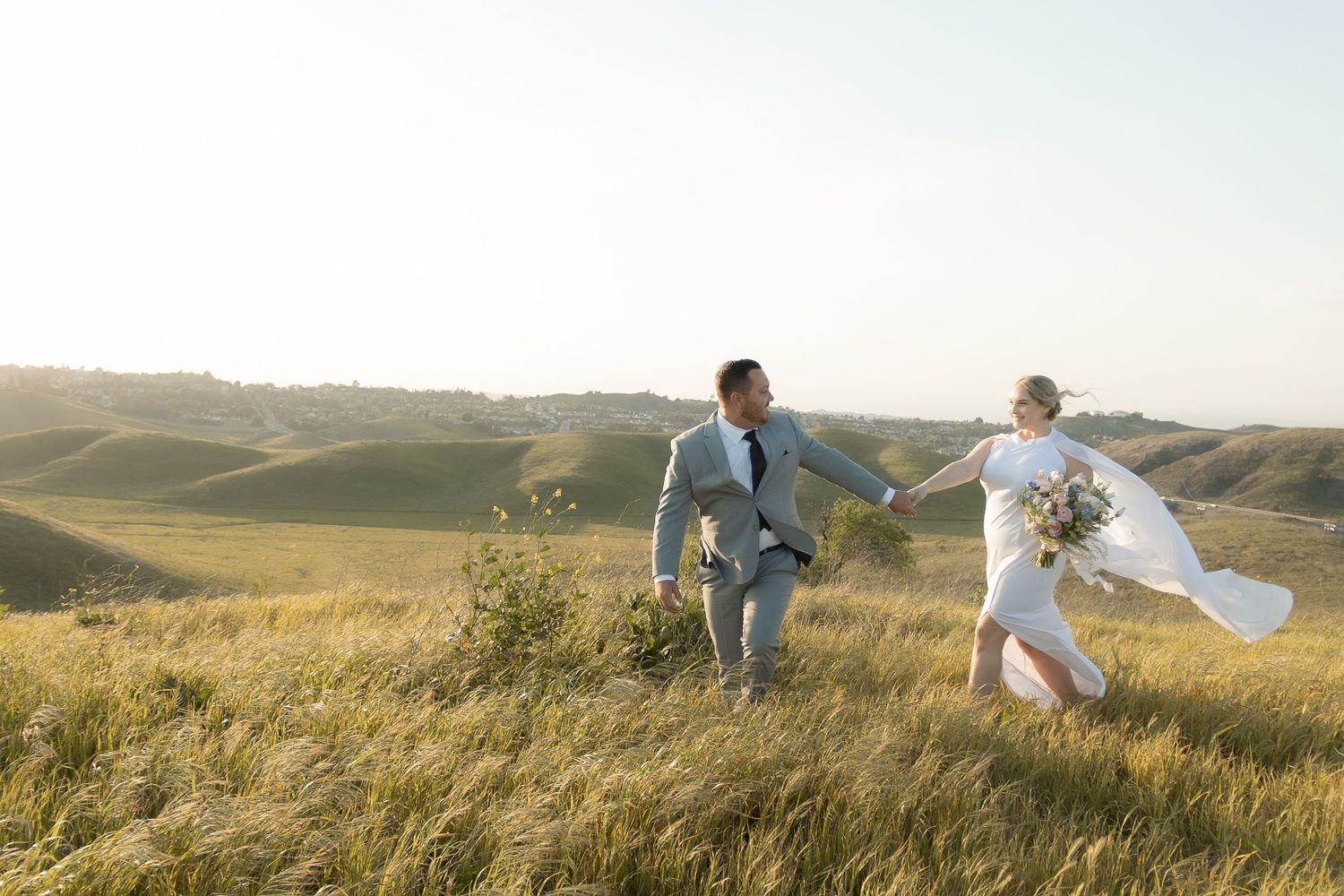 Couple posing in golden grass field during sunset photoshoot.