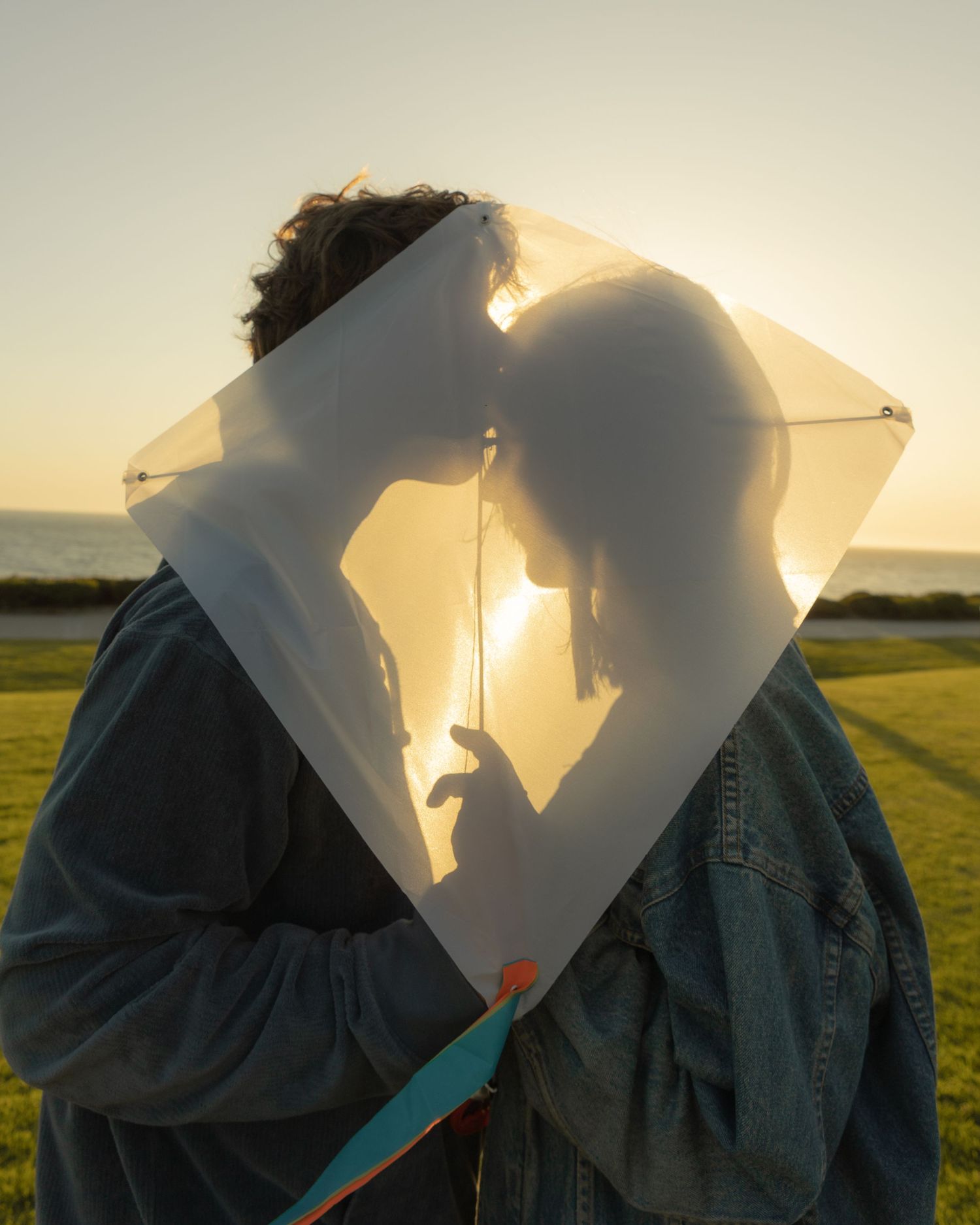 Silhouettes behind a kite create dramatic shadows at sunset.