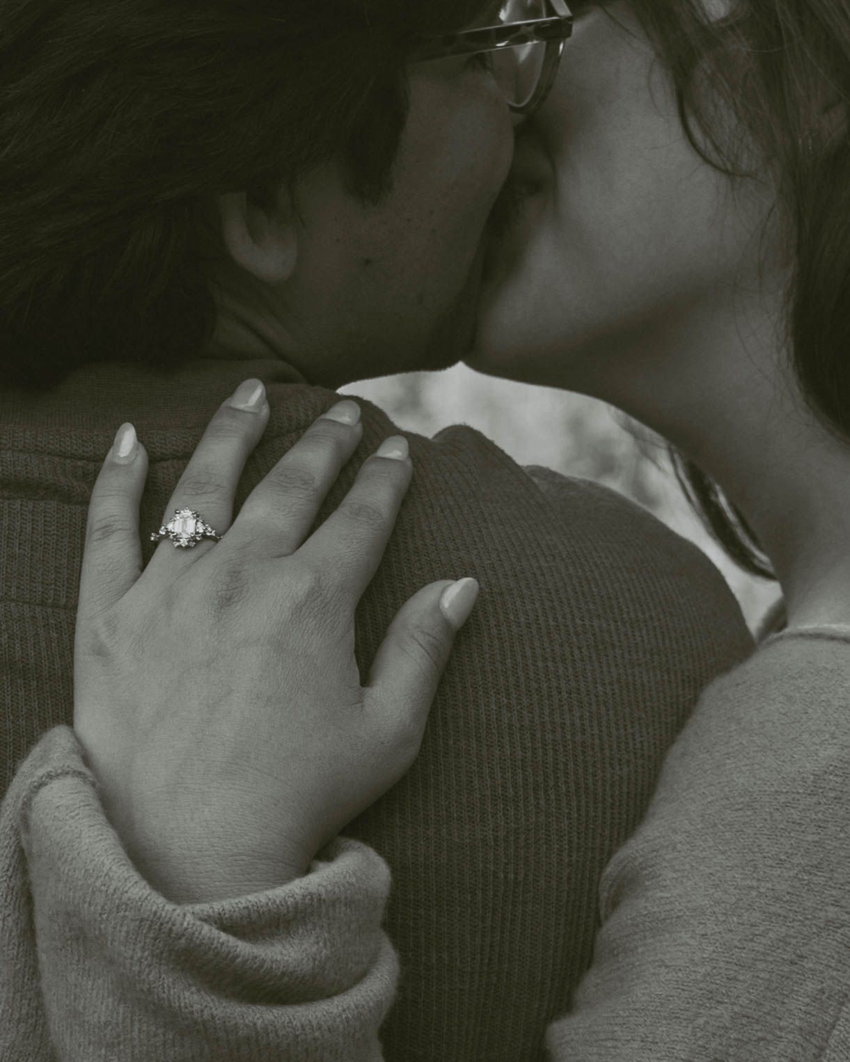 Black and white photo of a couple embracing, woman wearing a diamond engagement ring on her hand.