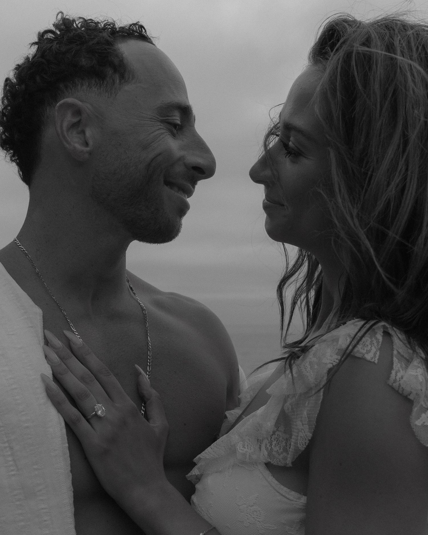 A couple shares an intimate black and white moment by the ocean.