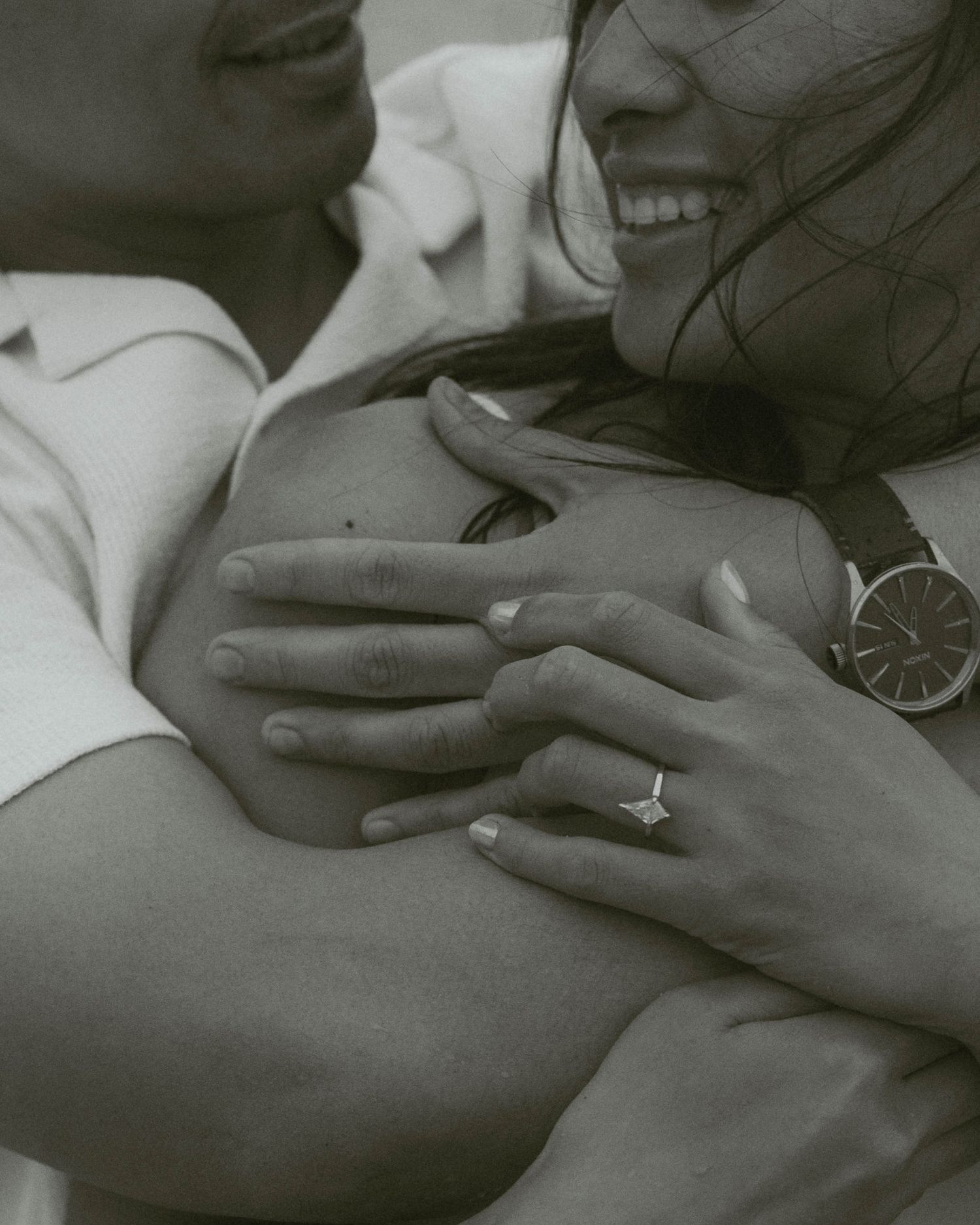 Close-up black and white photo of couple embracing, showing engagement ring on woman's hand.