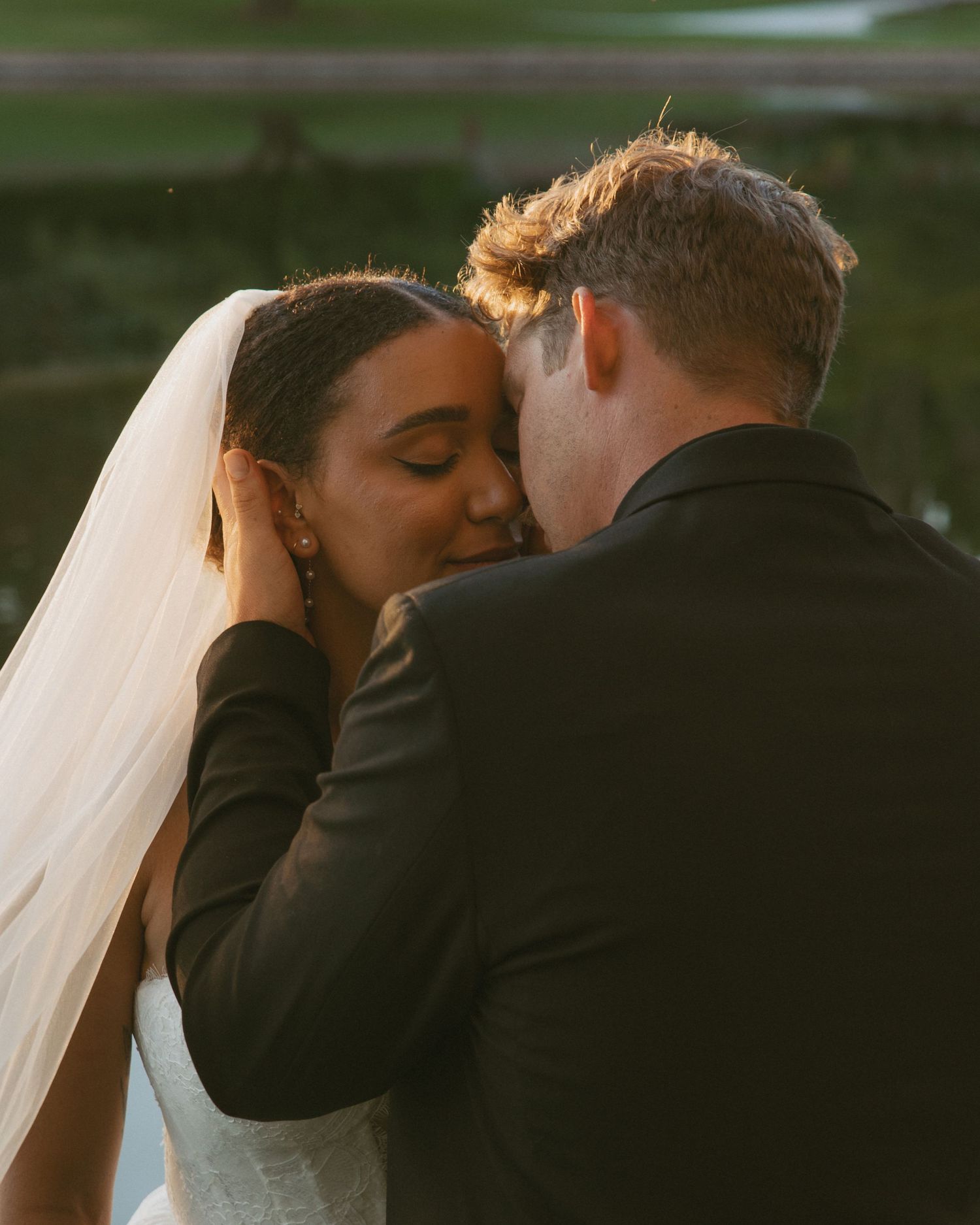 Intimate golden hour portrait of bride and groom touching foreheads tenderly after outdoor wedding.