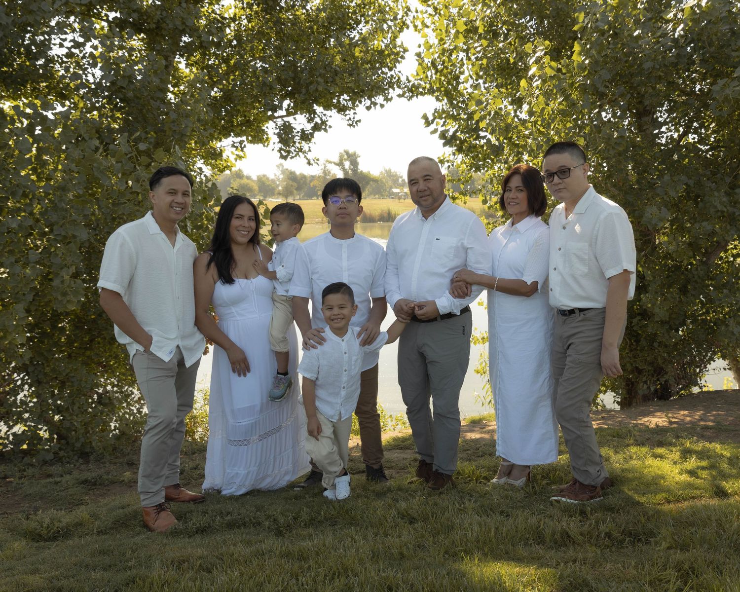 A group dressed in white sits together on a grassy hill during golden hour.