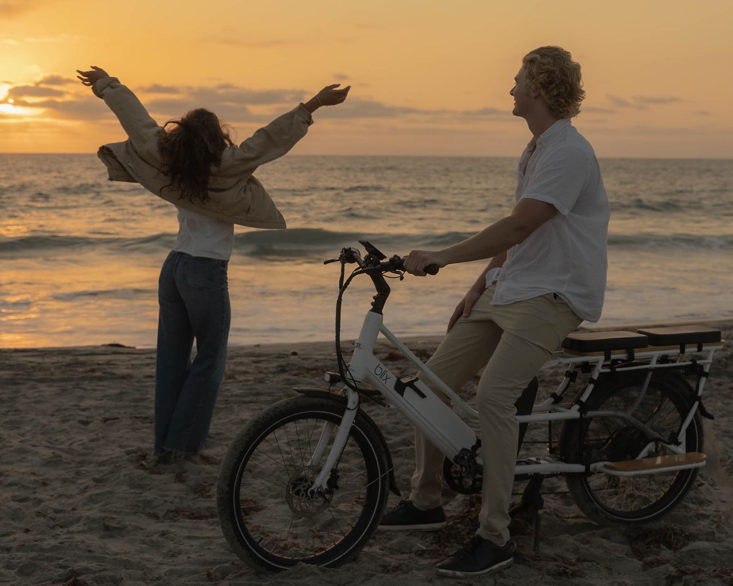 Silhouettes of people with a bicycle on beach during a vibrant orange sunset.