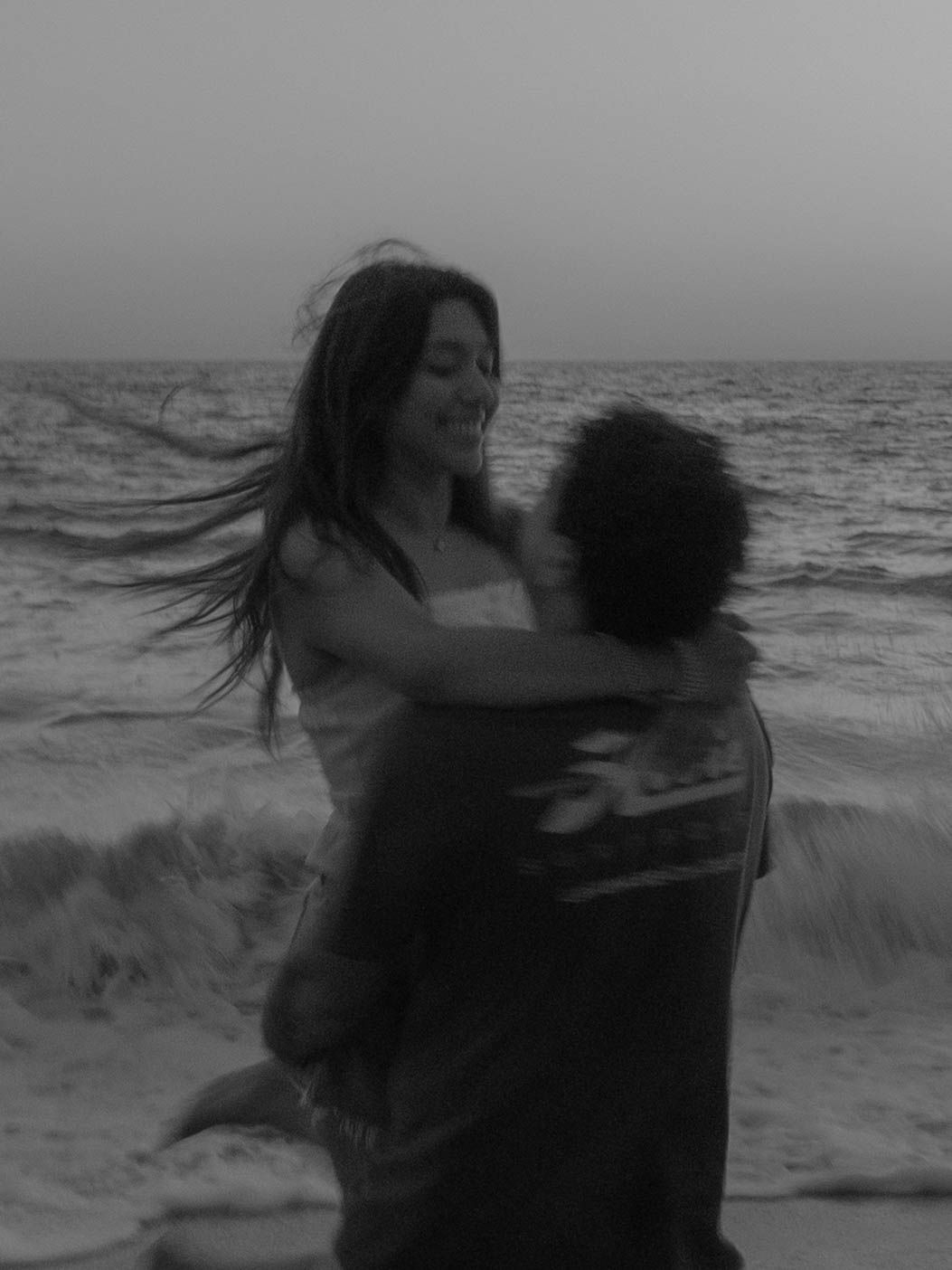 Silhouettes of a couple dancing and embracing by the ocean waves at dusk.