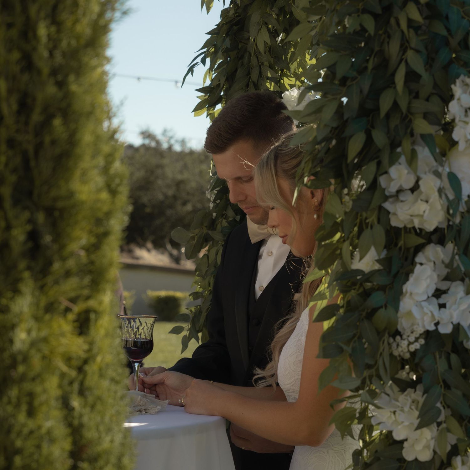 Wedding guests signing documents under floral decorations outdoors.