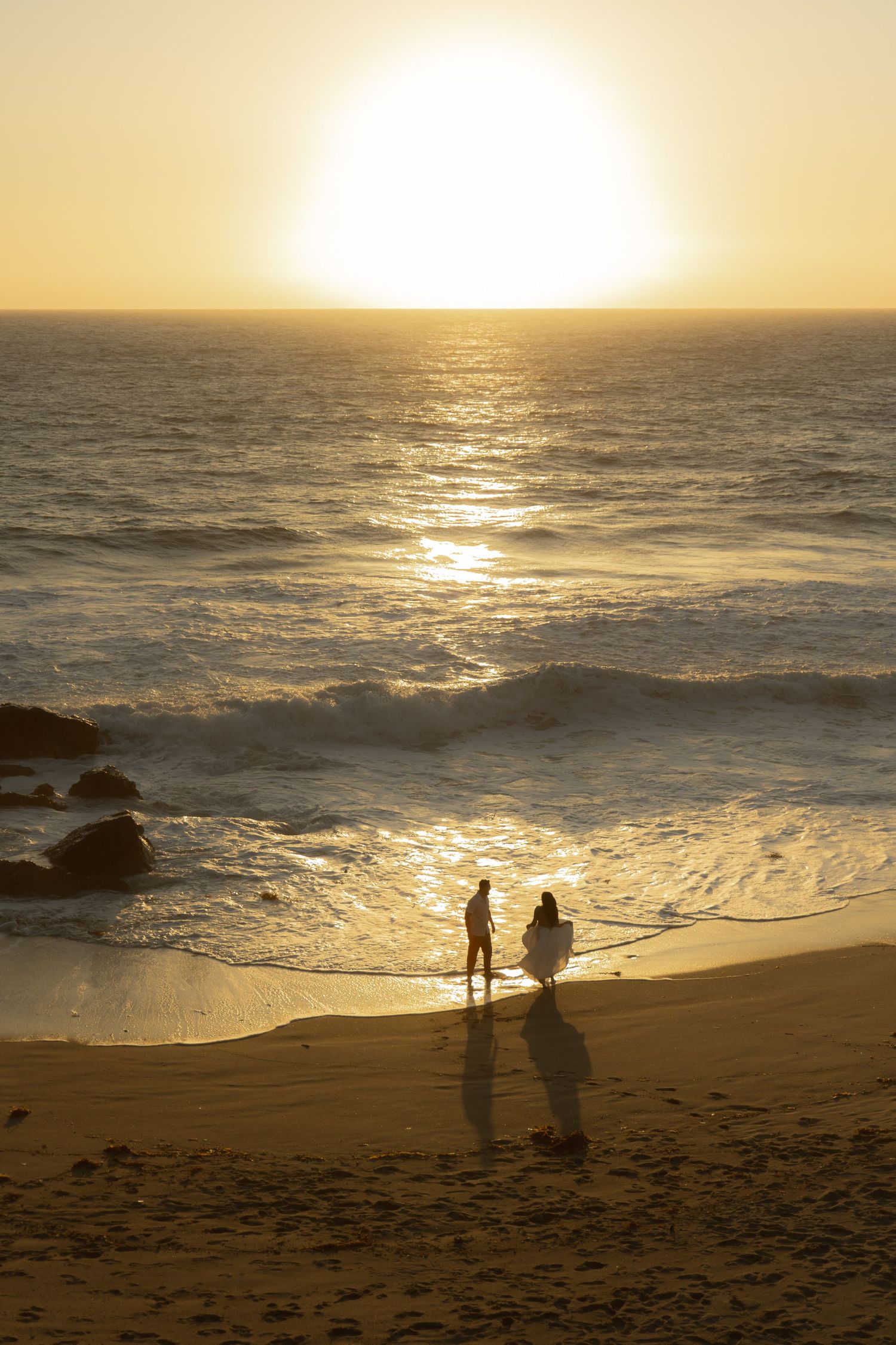 Silhouettes of people walking along a beach at sunset with golden light reflecting off the ocean waves and sand.