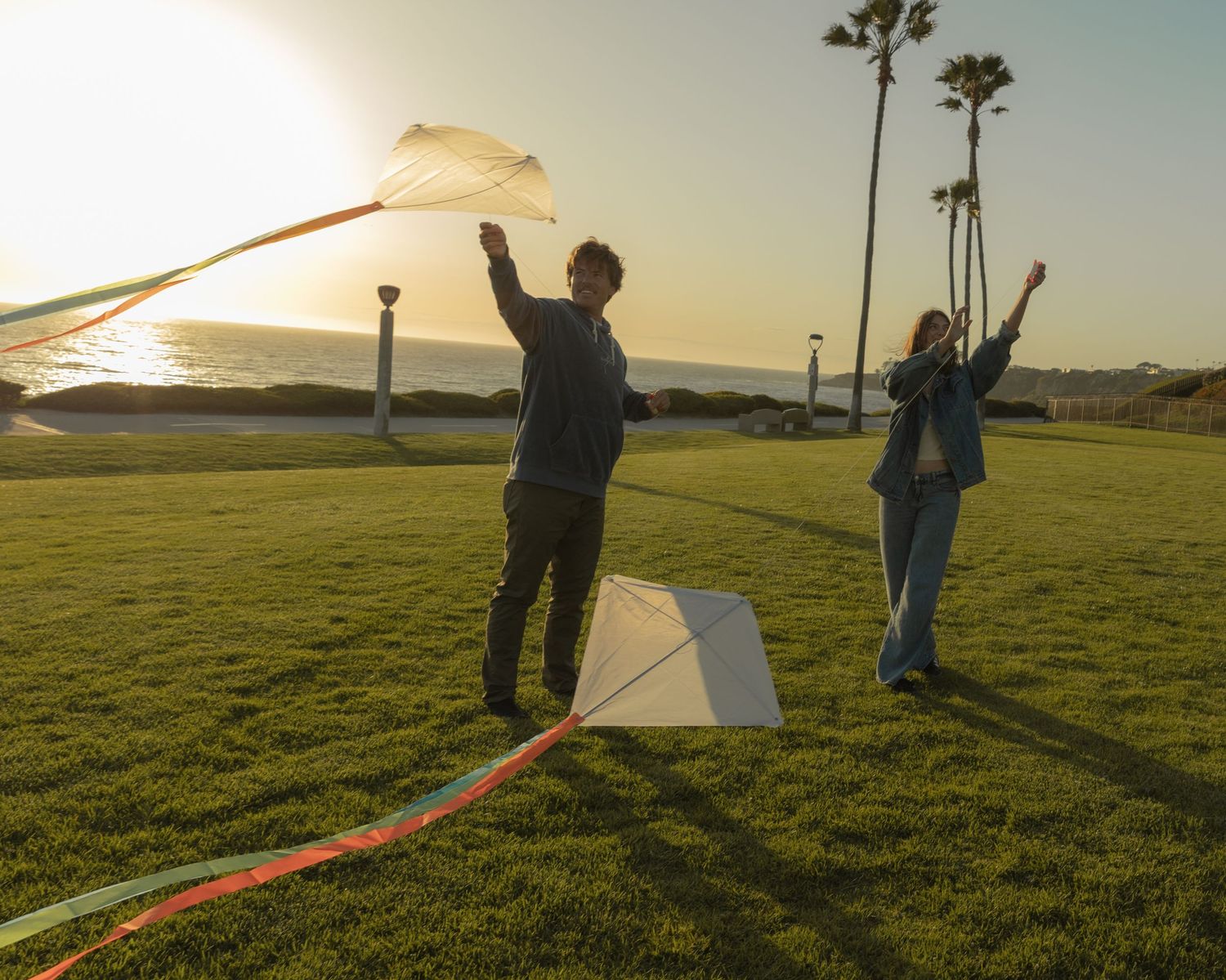 People play with a white kite in a grassy field during golden hour.