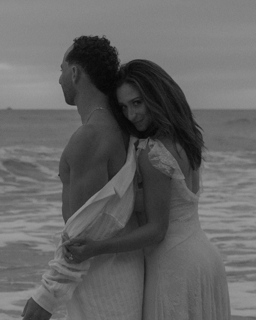 A romantic black and white beach photoshoot with two people embracing by the water.