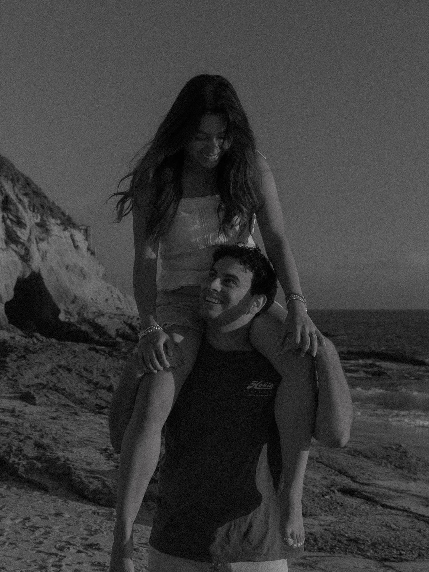 A romantic couple embraces on a rocky beach during sunset.
