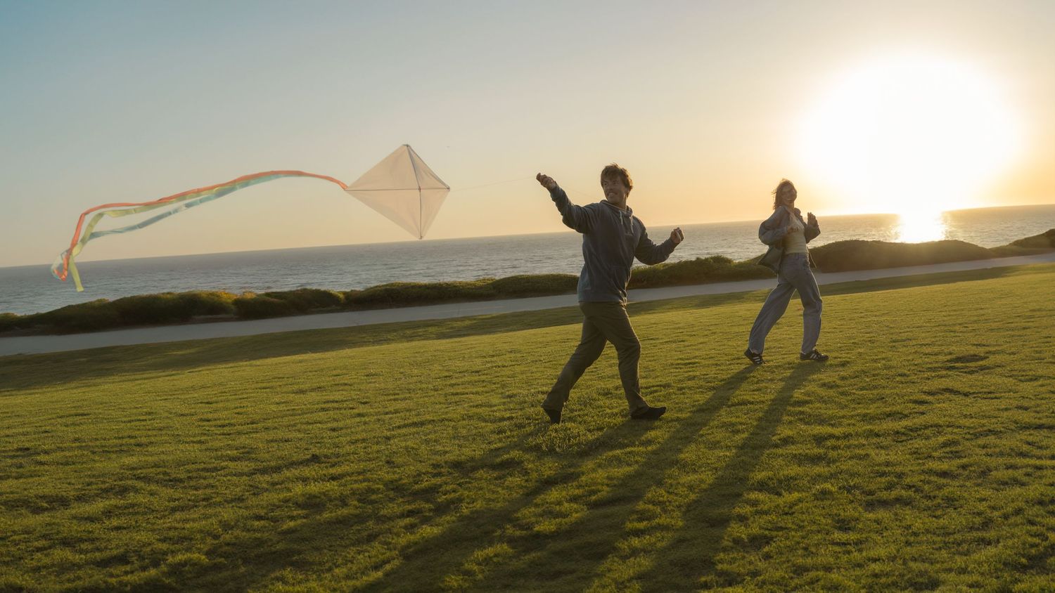 Silhouettes of people running with kites in a field at sunset.