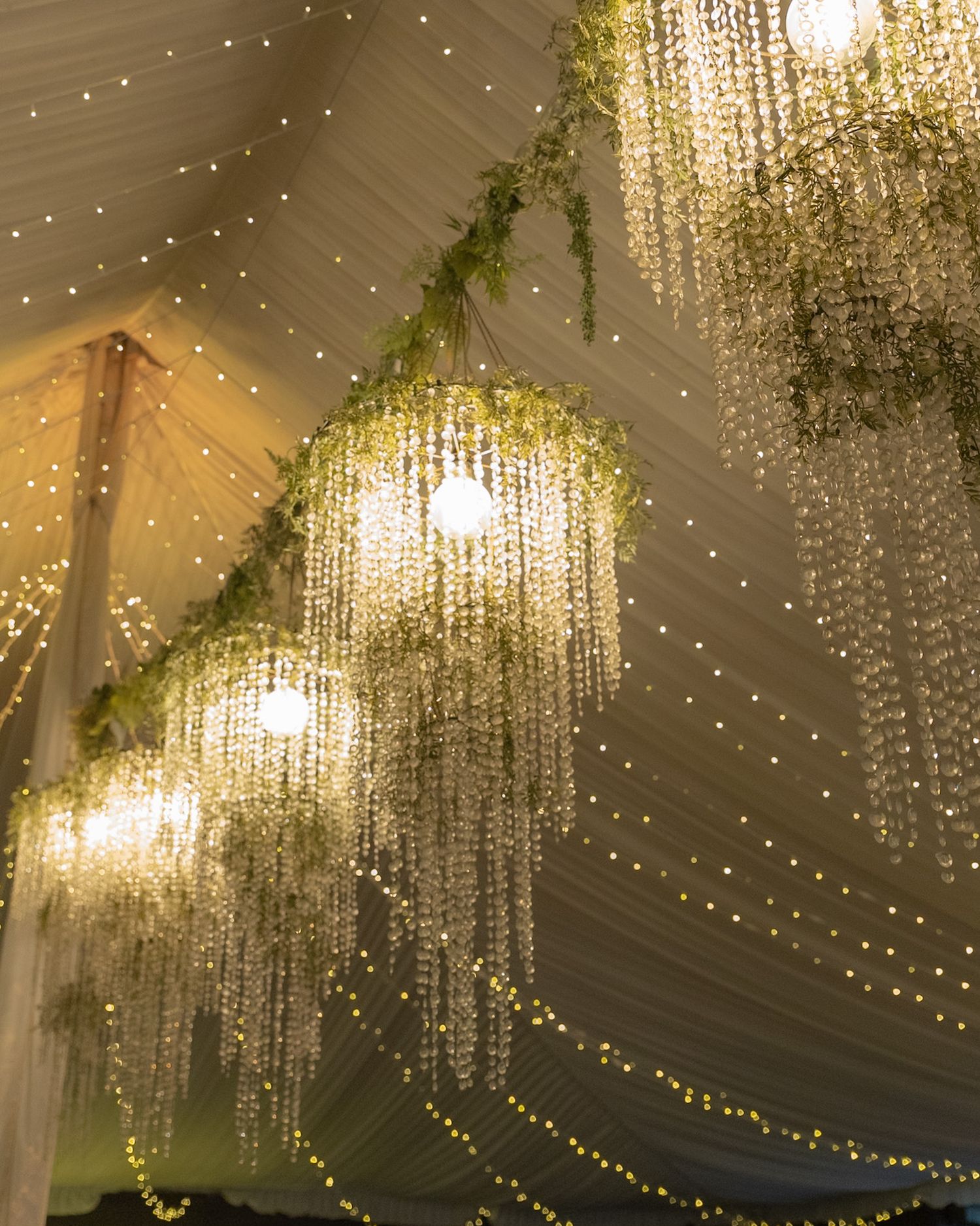 Elegant wedding tent ceiling adorned with cascading floral chandeliers and warm fairy lights.