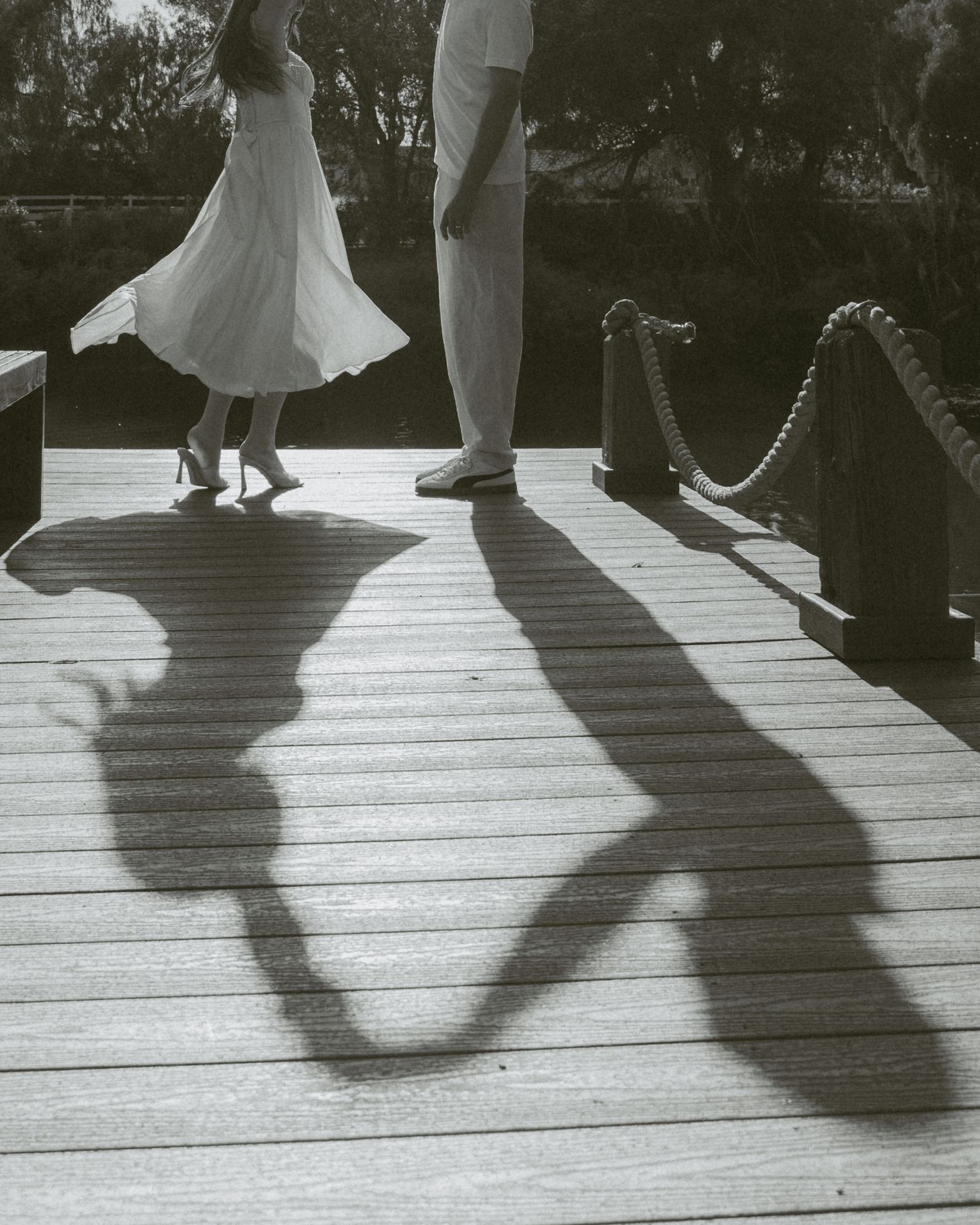 Black and white photo of a couple holding hands on a wooden deck, their romantic shadows cast on the boards.