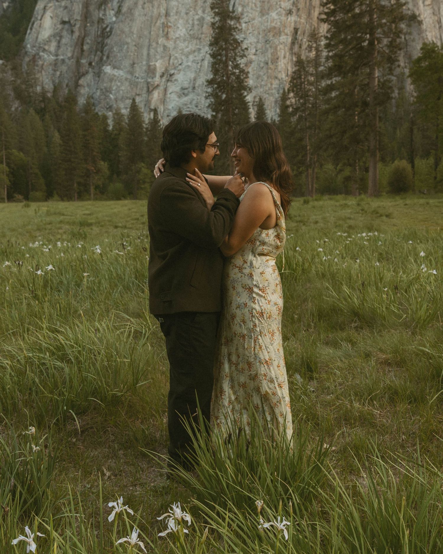 Couple embracing in a wildflower meadow with tall pine trees and granite cliffs in Yosemite National Park.