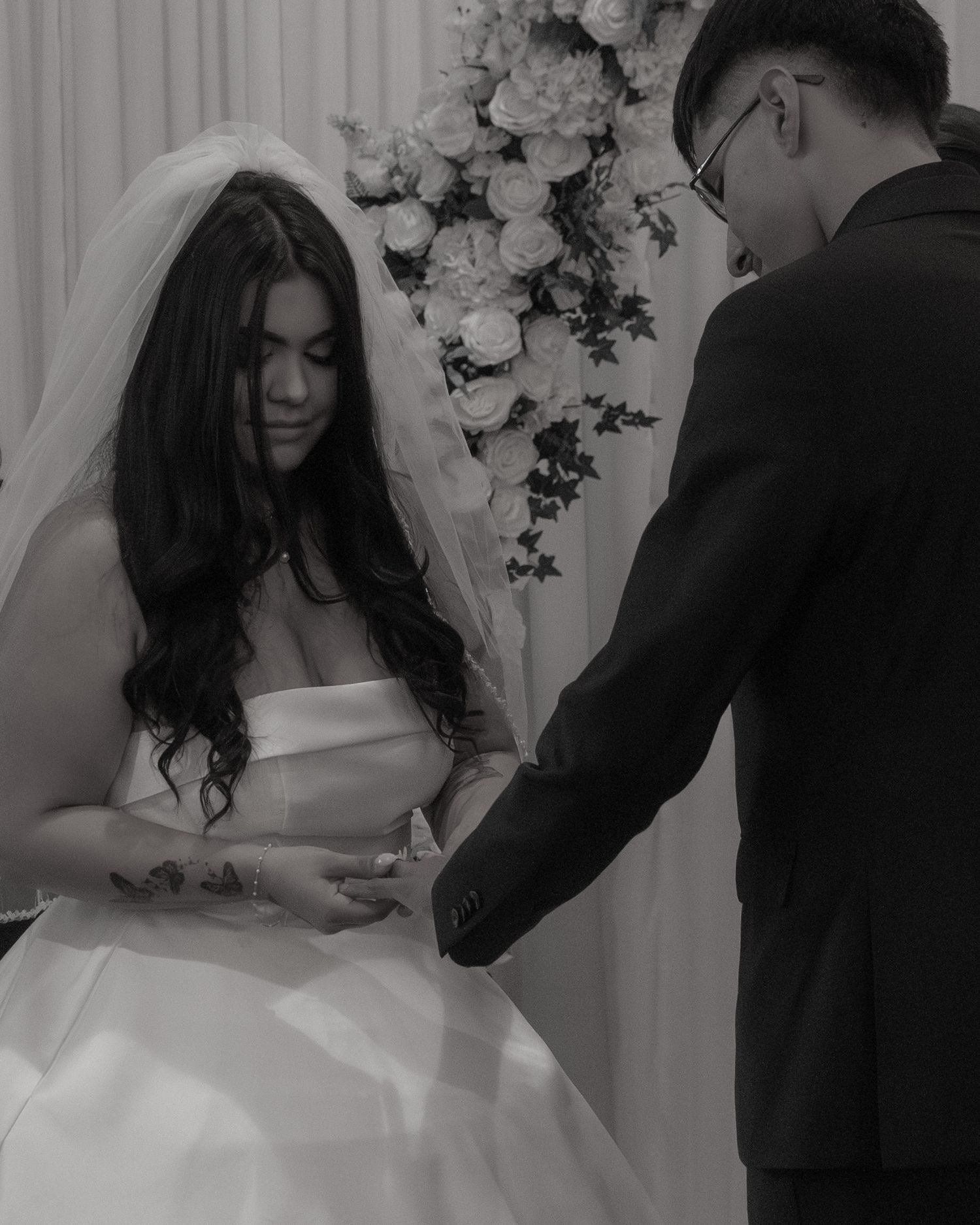 Black and white photos of couple signing wedding documents under floral arch.