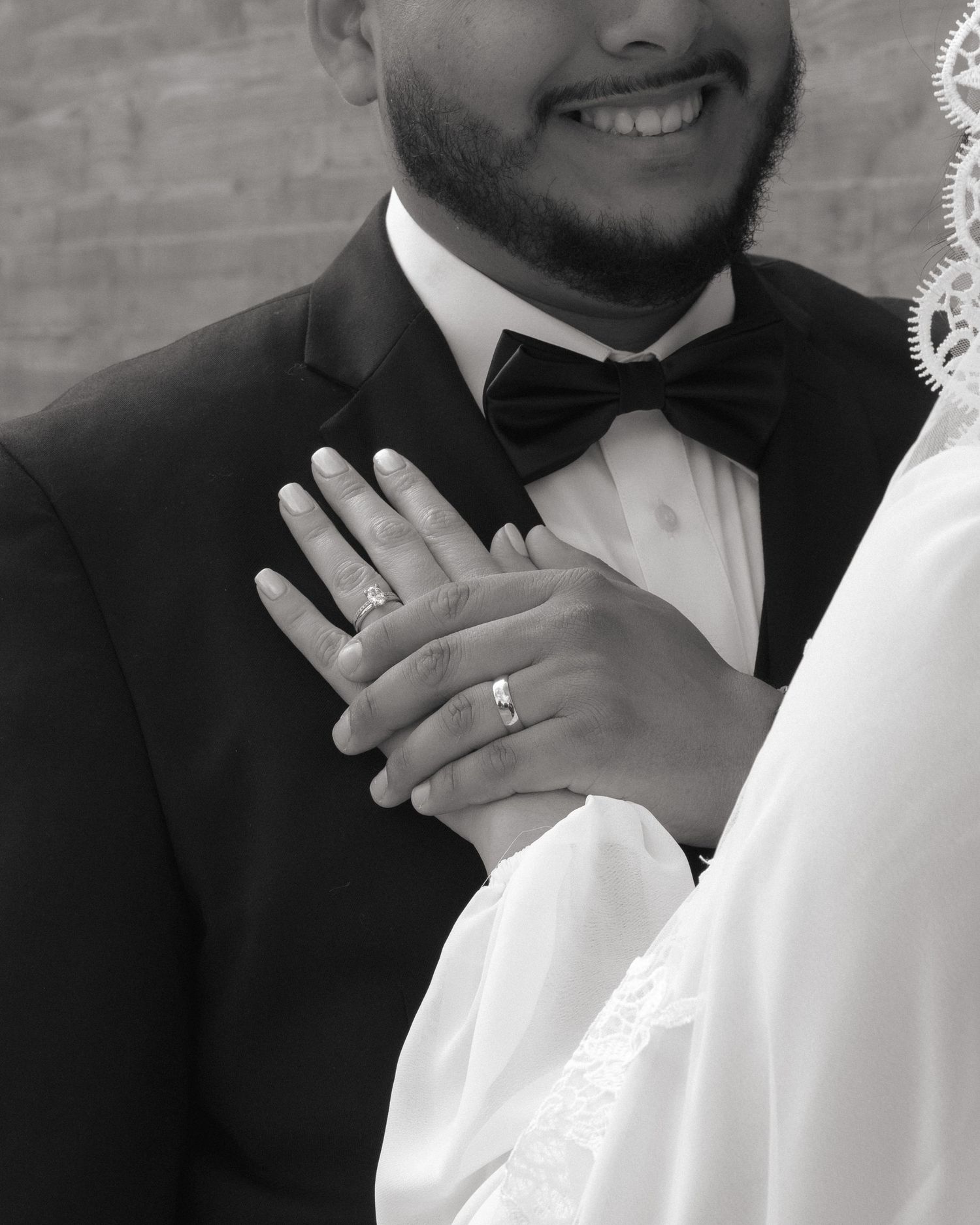 Black and white close-up of newlyweds wedding rings as bride places hands on grooms tuxedo chest.