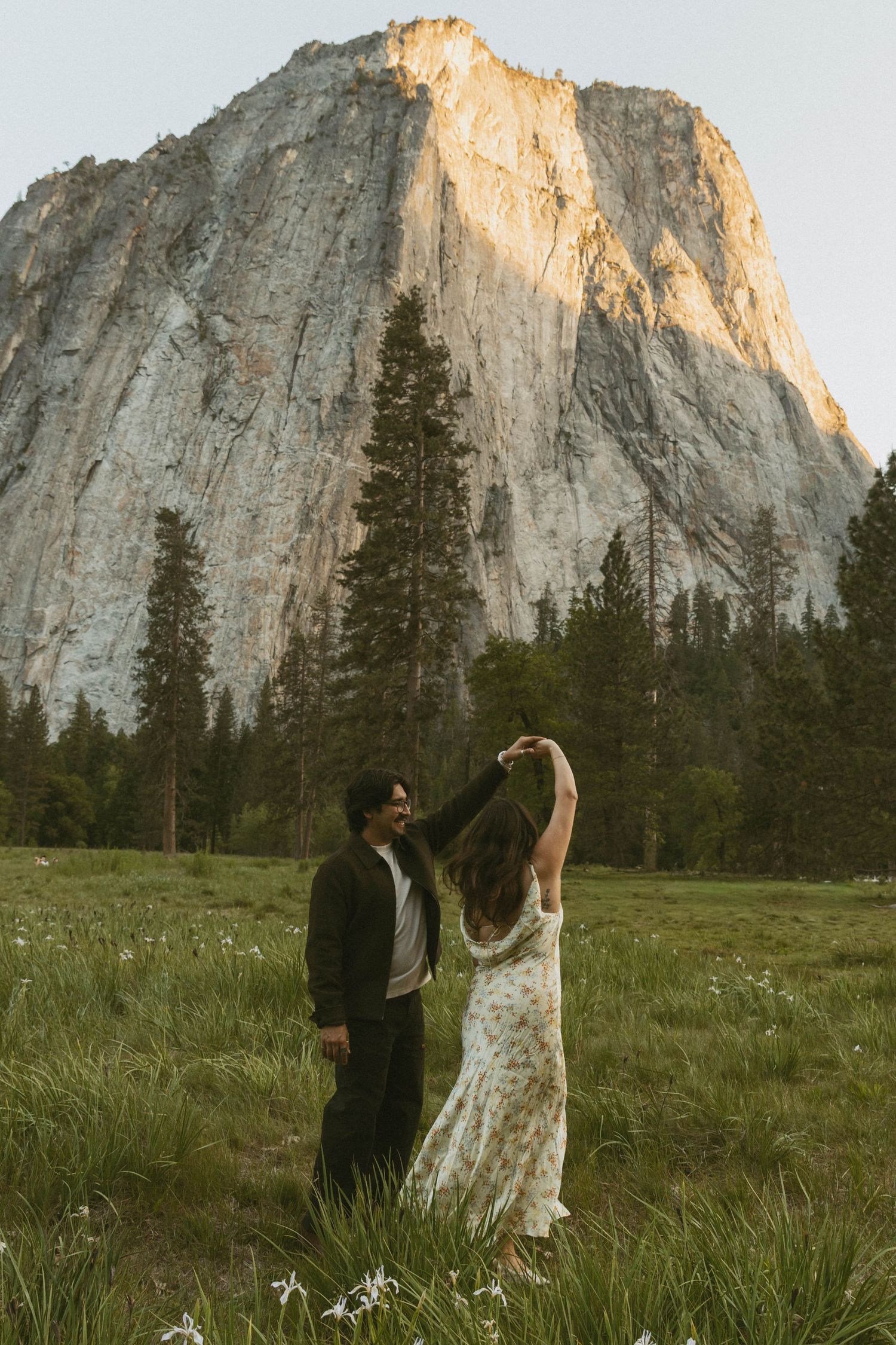 Couple dancing in Yosemite meadow with El Capitan granite wall and pine trees in background at sunset.