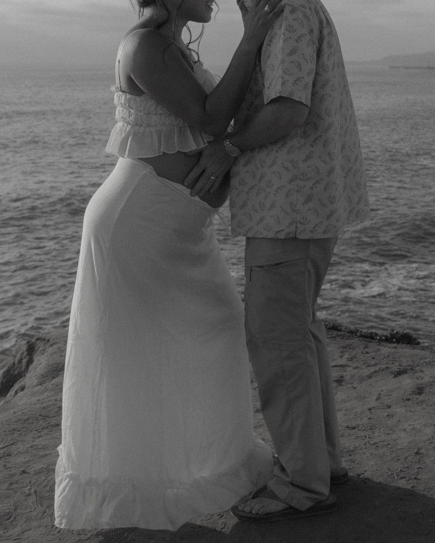 A couple shares an intimate moment during their beach maternity photoshoot.