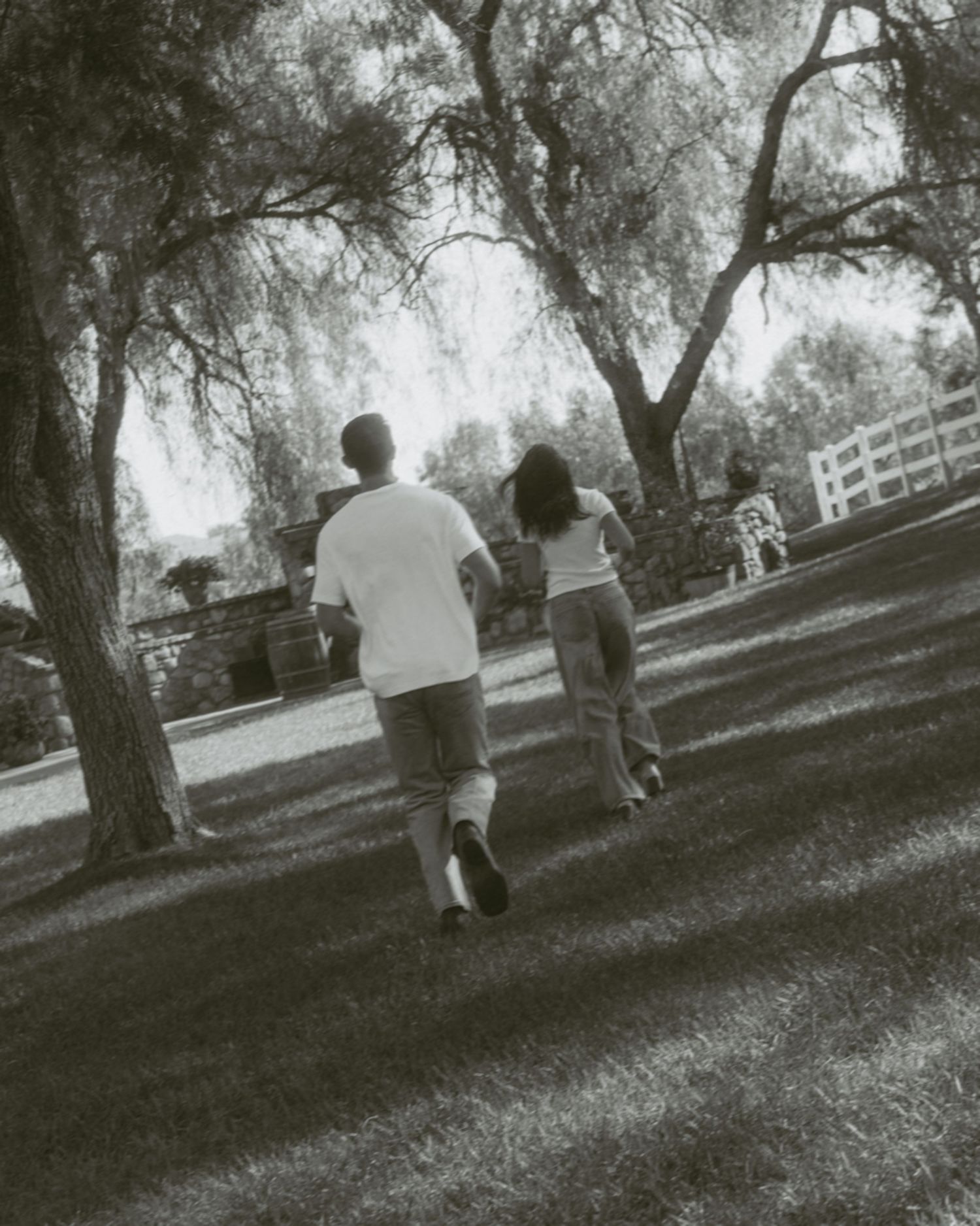 Black and white photo of two people walking uphill through a shaded park with large trees and green grass.