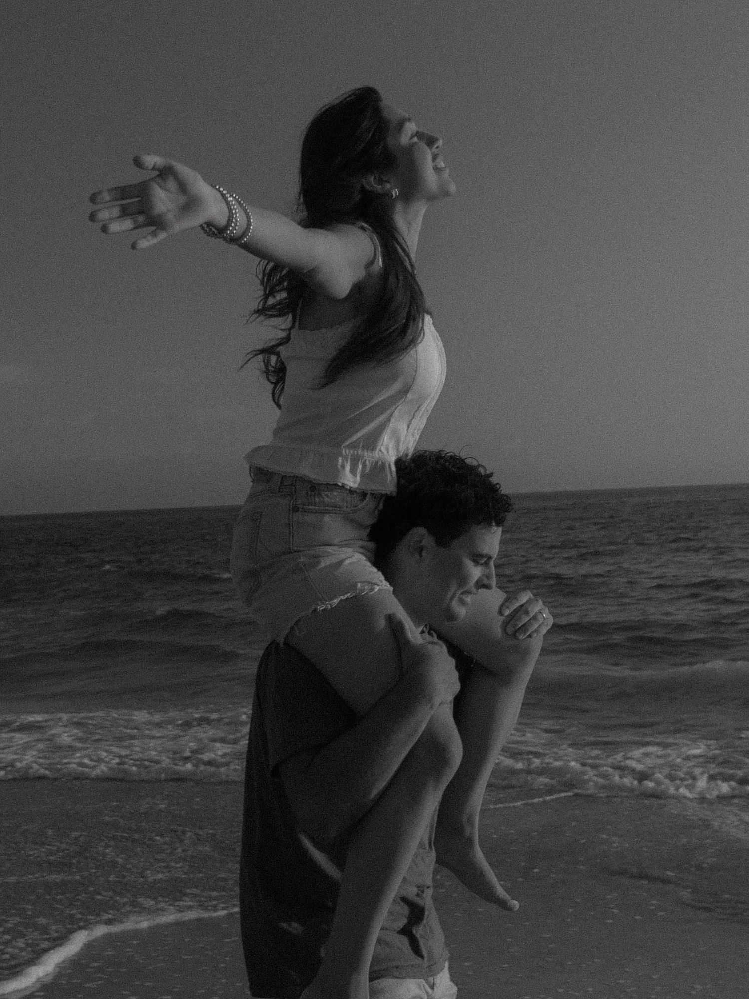A playful beach moment captured in black and white with someone riding on another's shoulders.