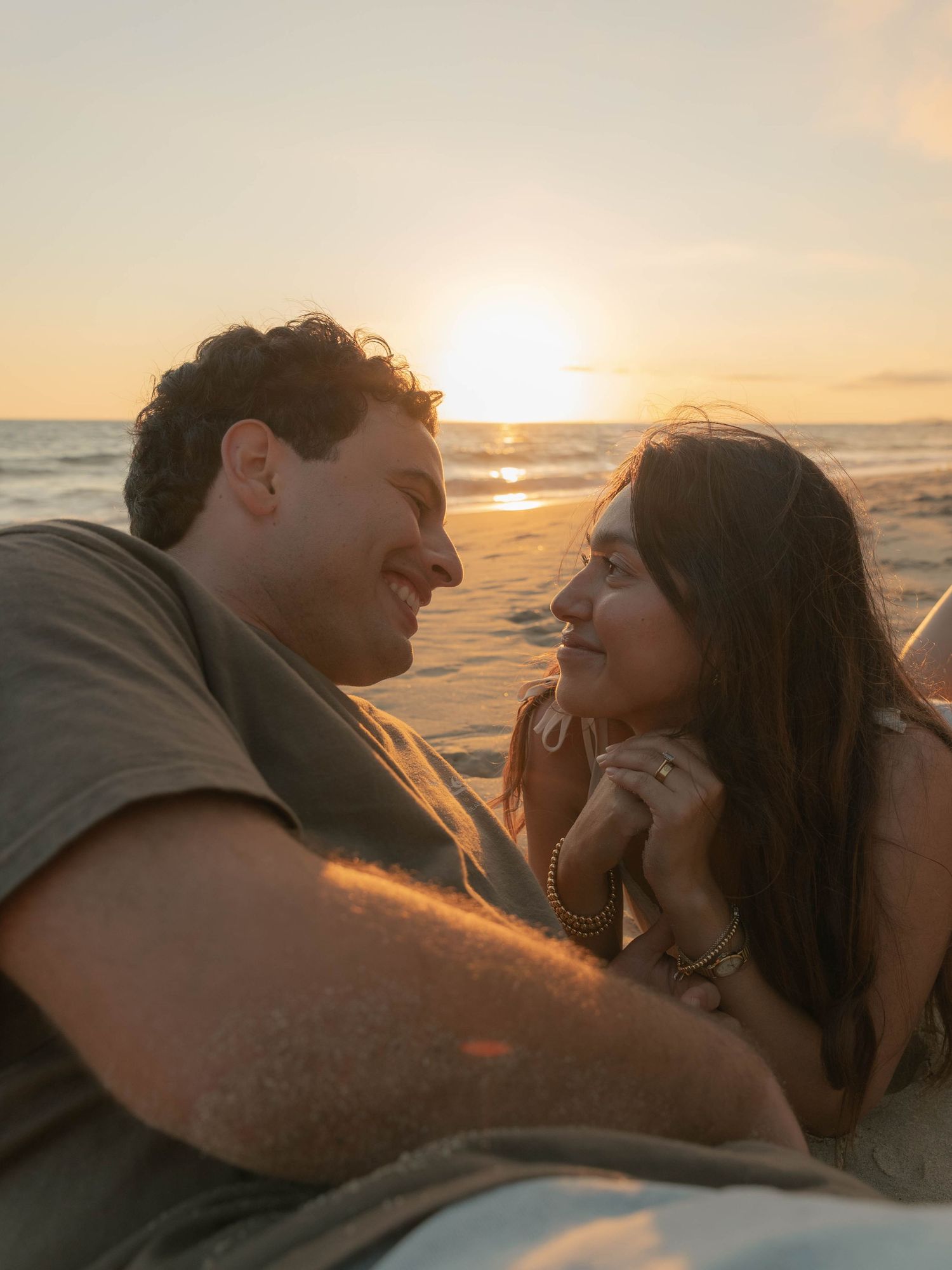 A romantic couple embraces on the beach during golden hour sunset.