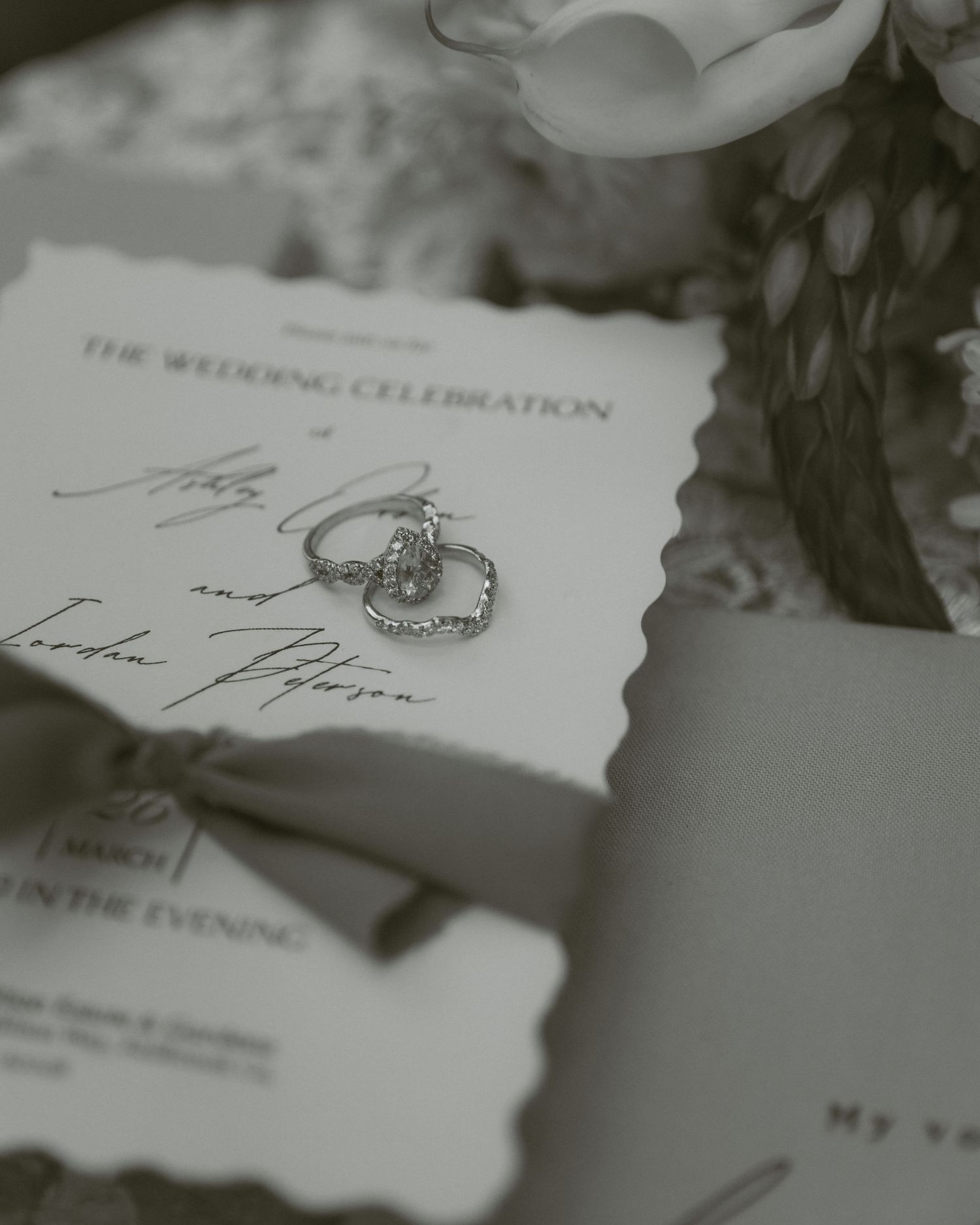 Black and white photo of wedding rings resting on elegant wedding invitation with script calligraphy.
