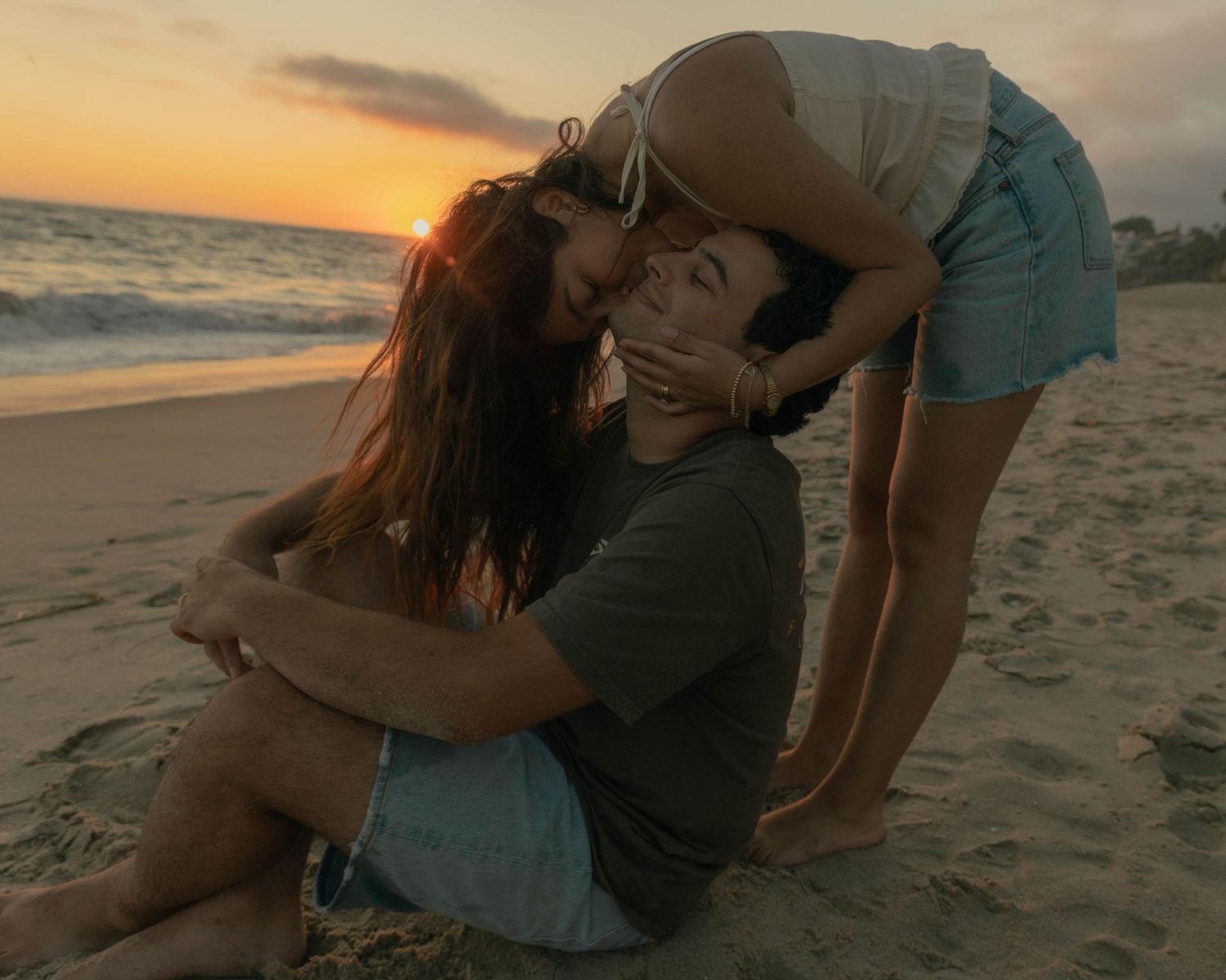 Two people share intimate moments on a sandy beach at golden hour.
