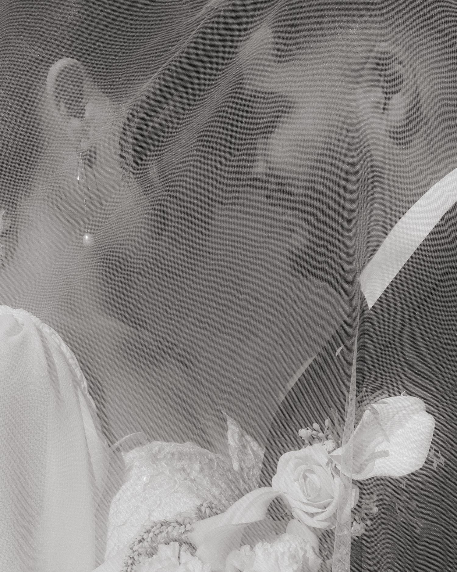 Romantic black and white portrait of bride and groom nearly kissing with rose boutonniere detail.