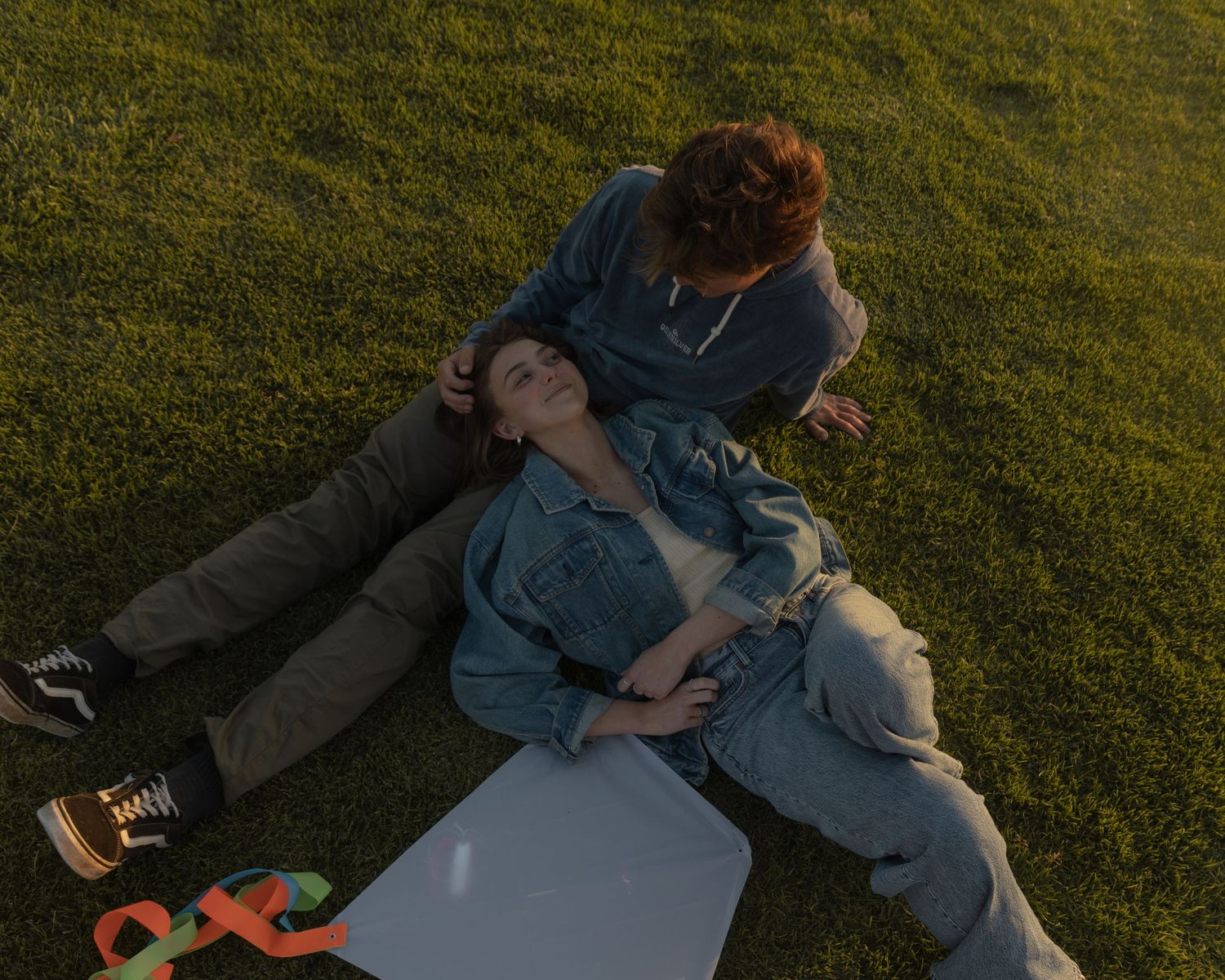 A couple relaxes on grass while reading books and enjoying a sunny afternoon outdoors.