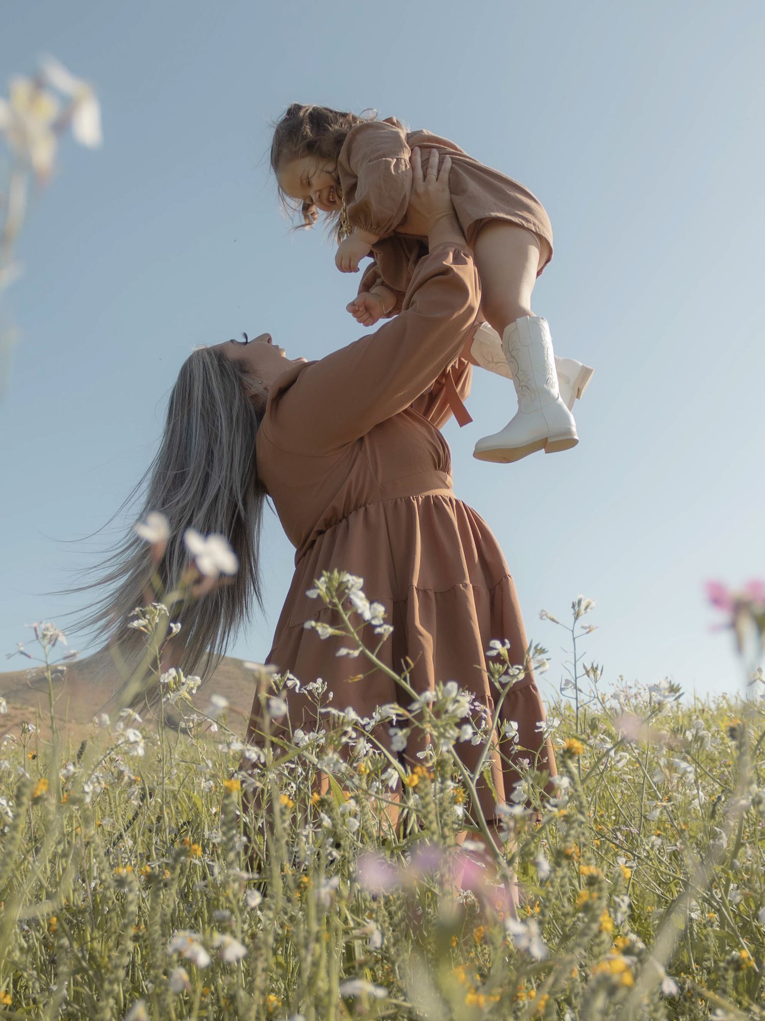 People in flowing dresses dancing through a wildflower meadow under blue summer skies.
