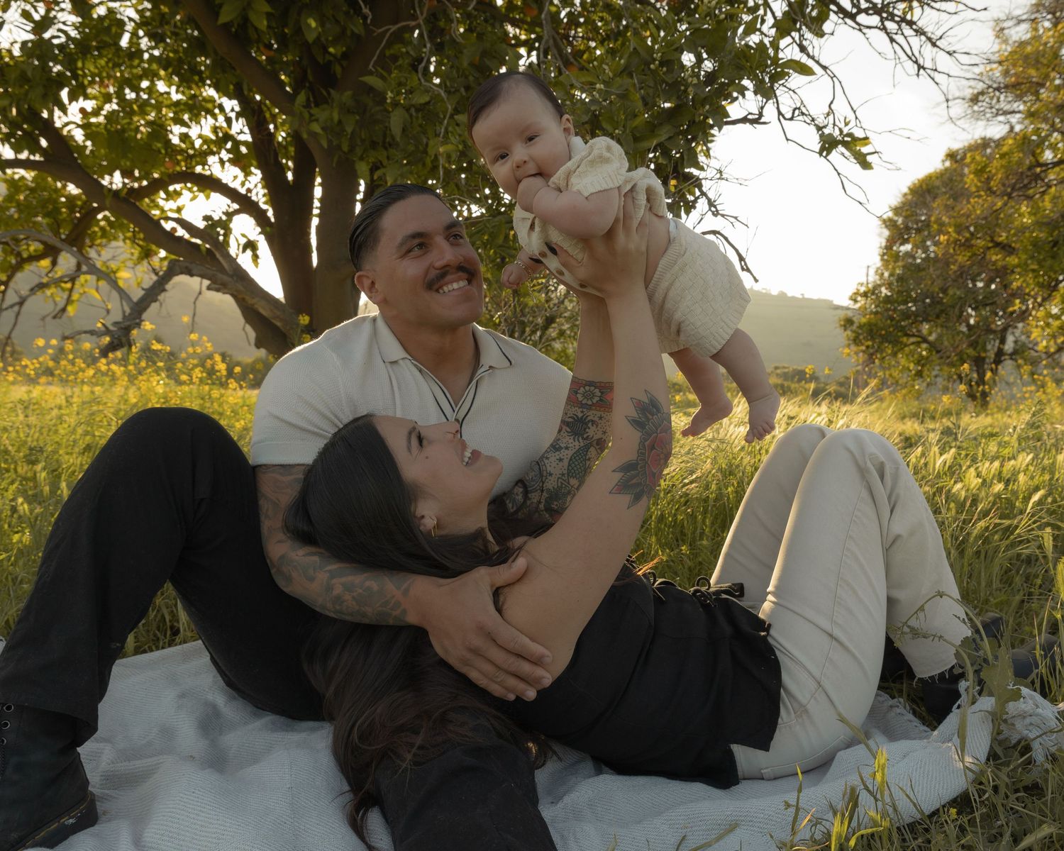 A tender moment between two people lying on grass surrounded by trees.