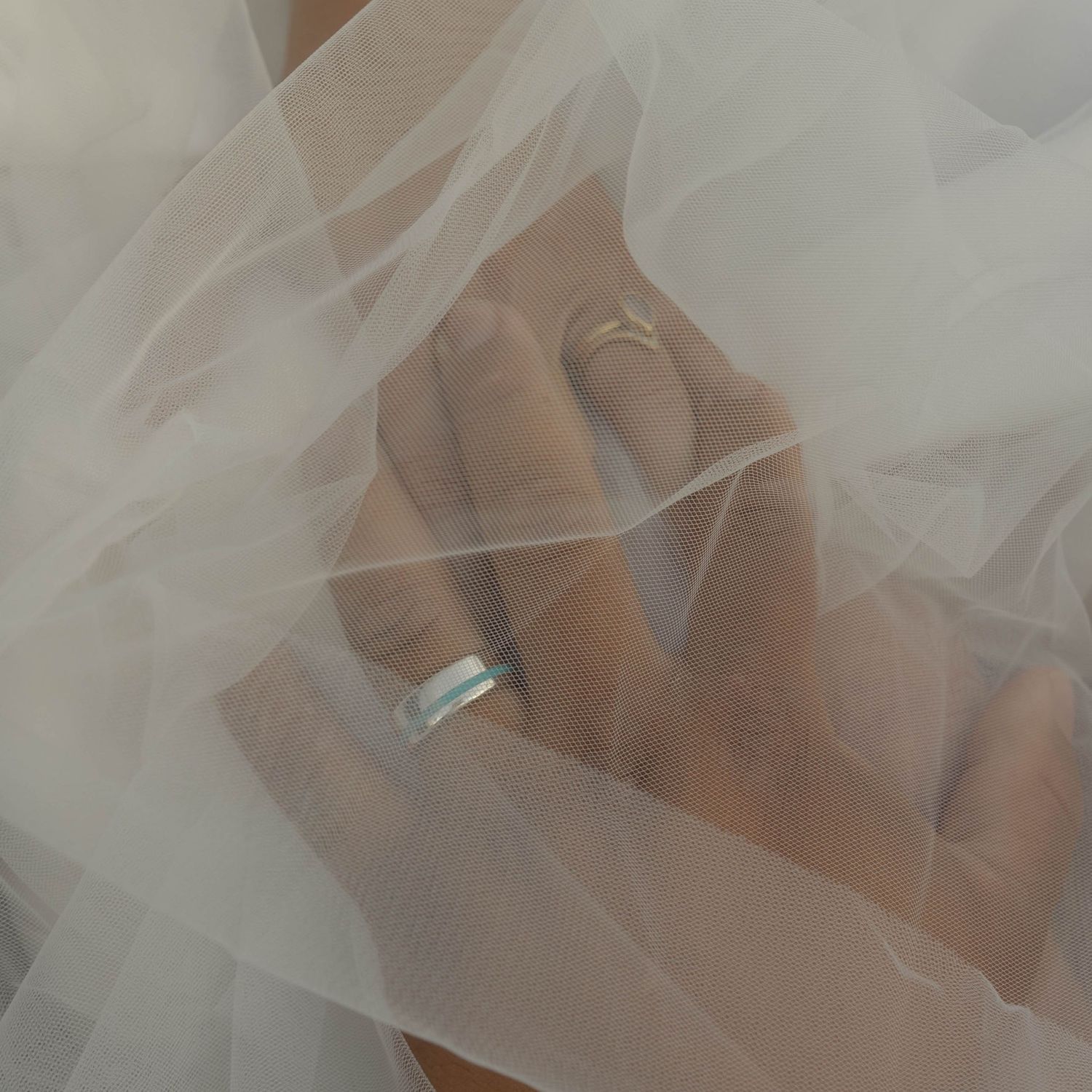 Close-up details of wedding rings through delicate white tulle veil fabric.