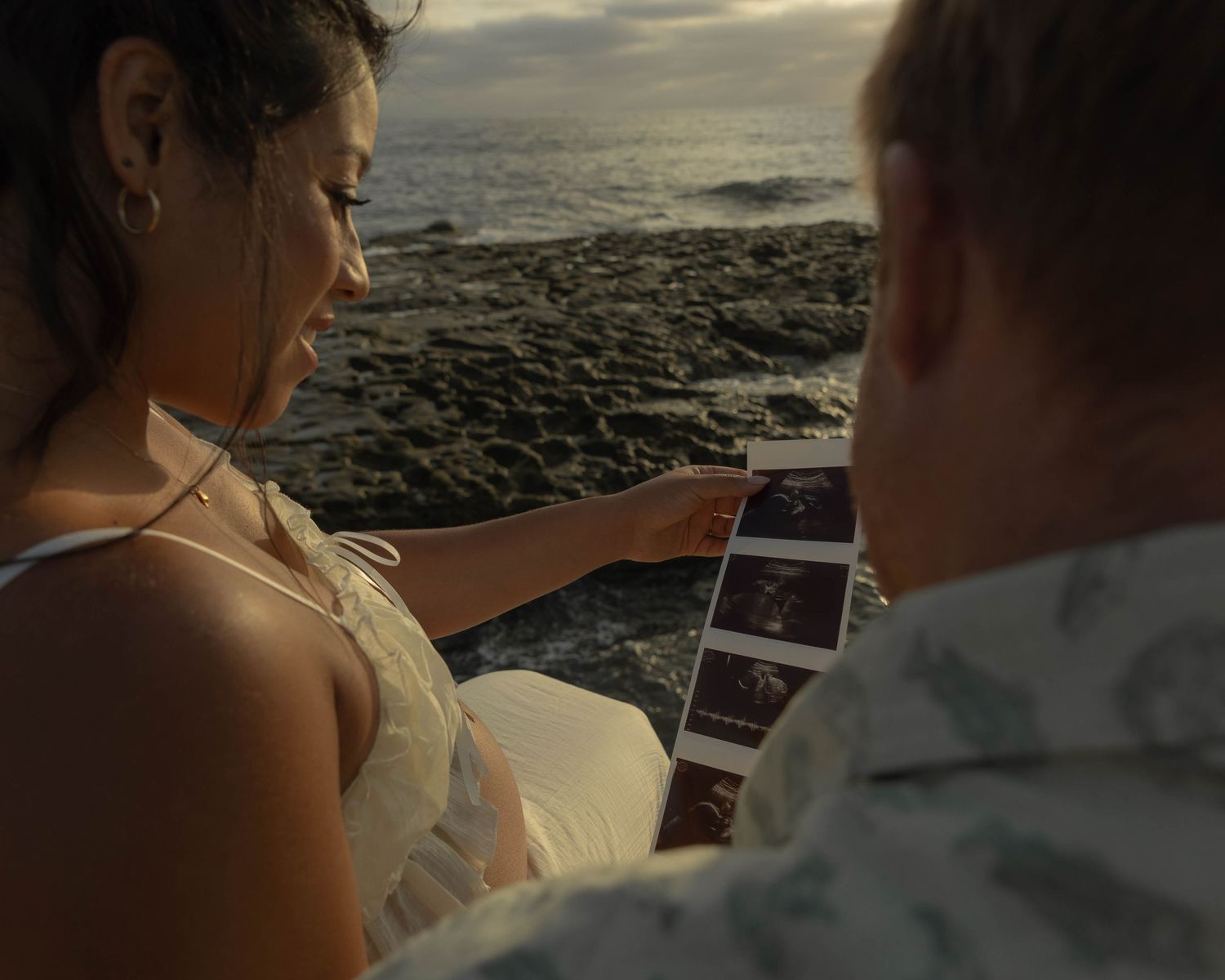 Two people looking at photographs together against an ocean sunset backdrop.