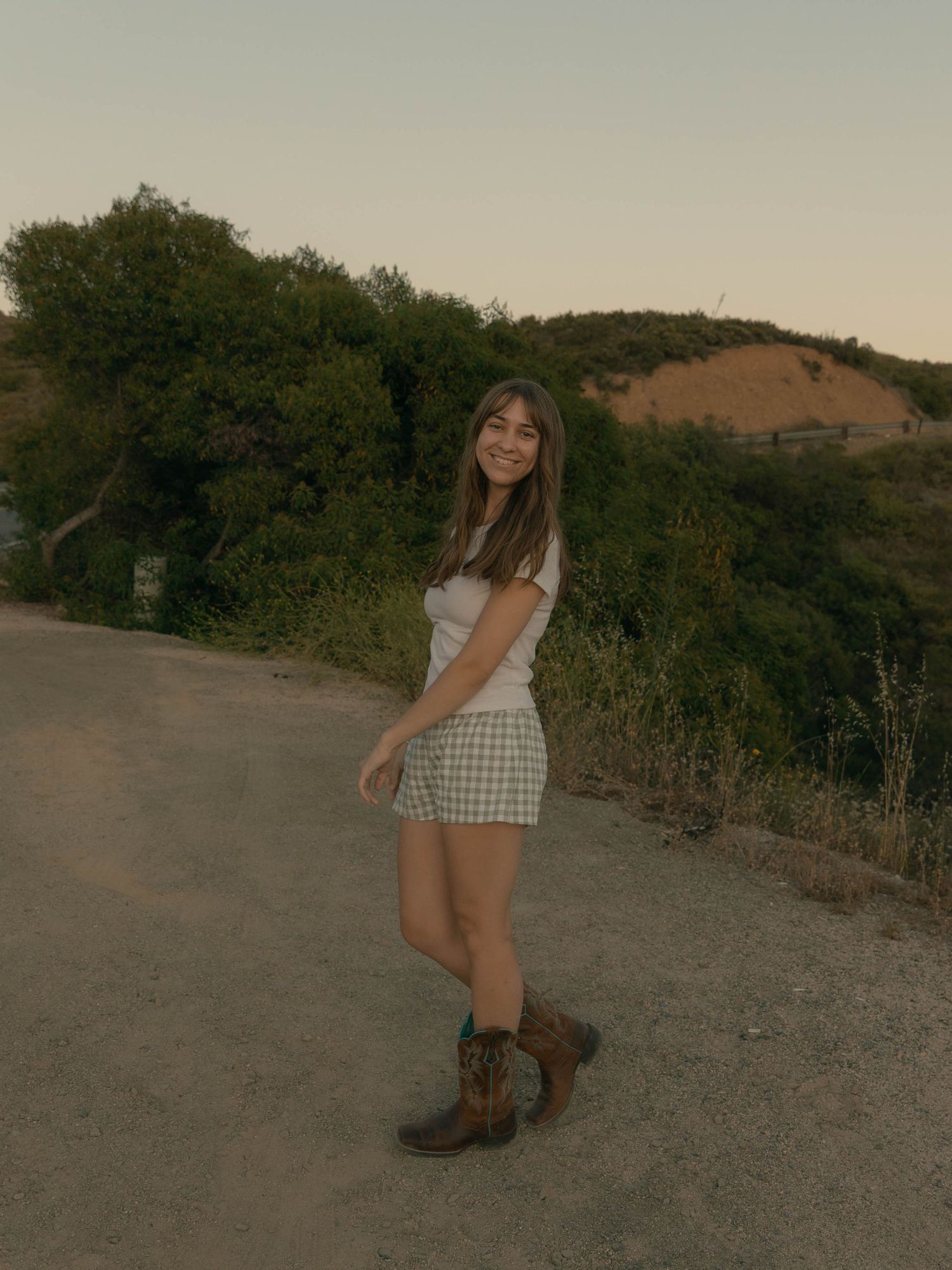 Person in casual attire striking fun poses on a natural trail during golden hour.