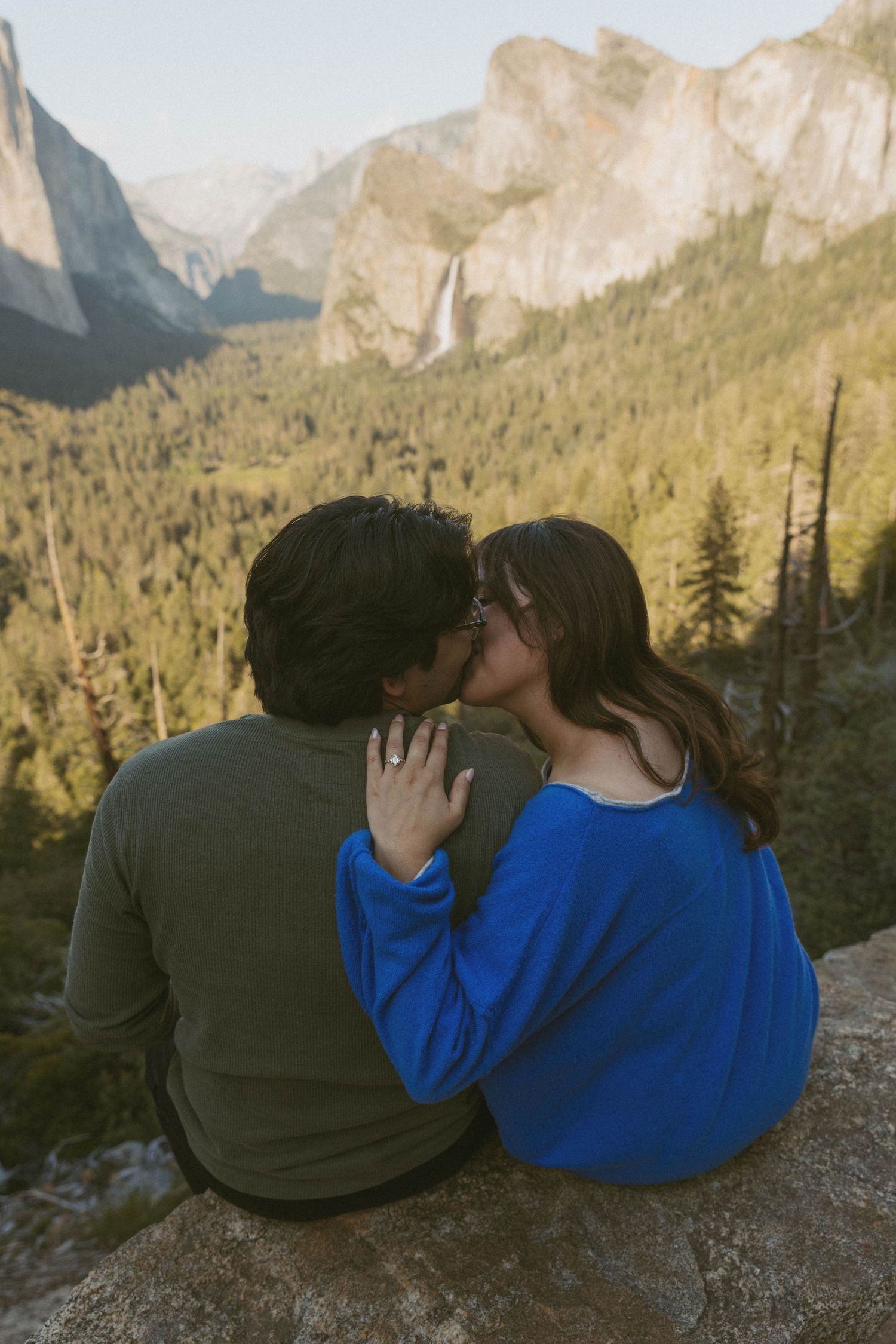 Couple sharing a romantic kiss on a rocky overlook with stunning Yosemite Valley and waterfall views.